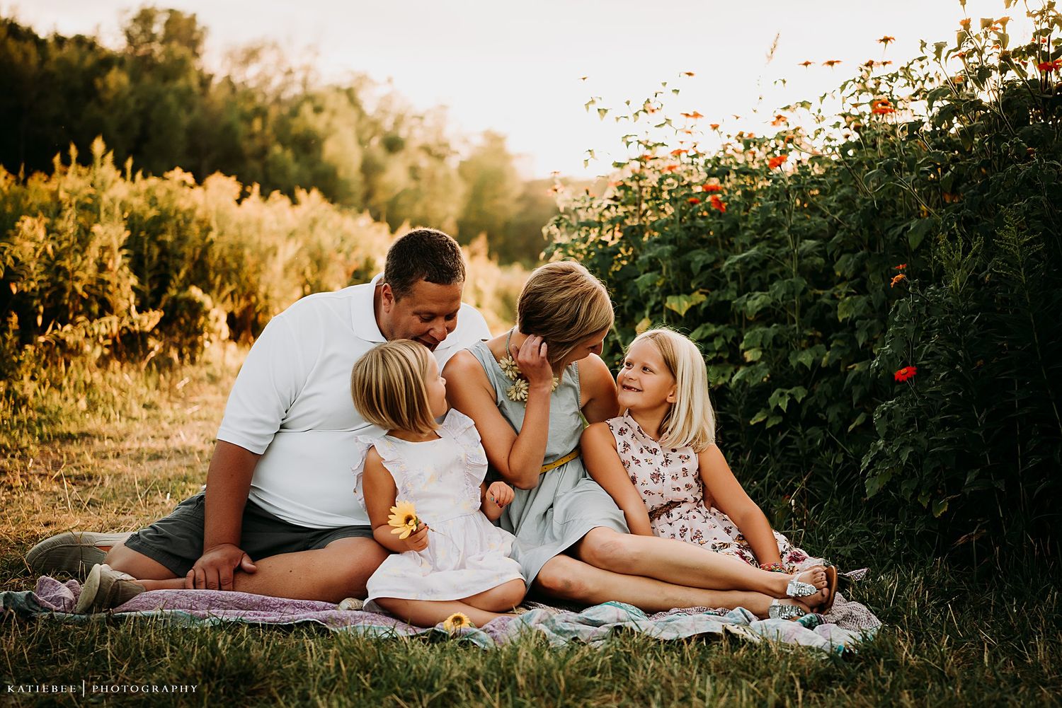 Family enjoying a summer evening picnic beside a flowering garden at sunset.