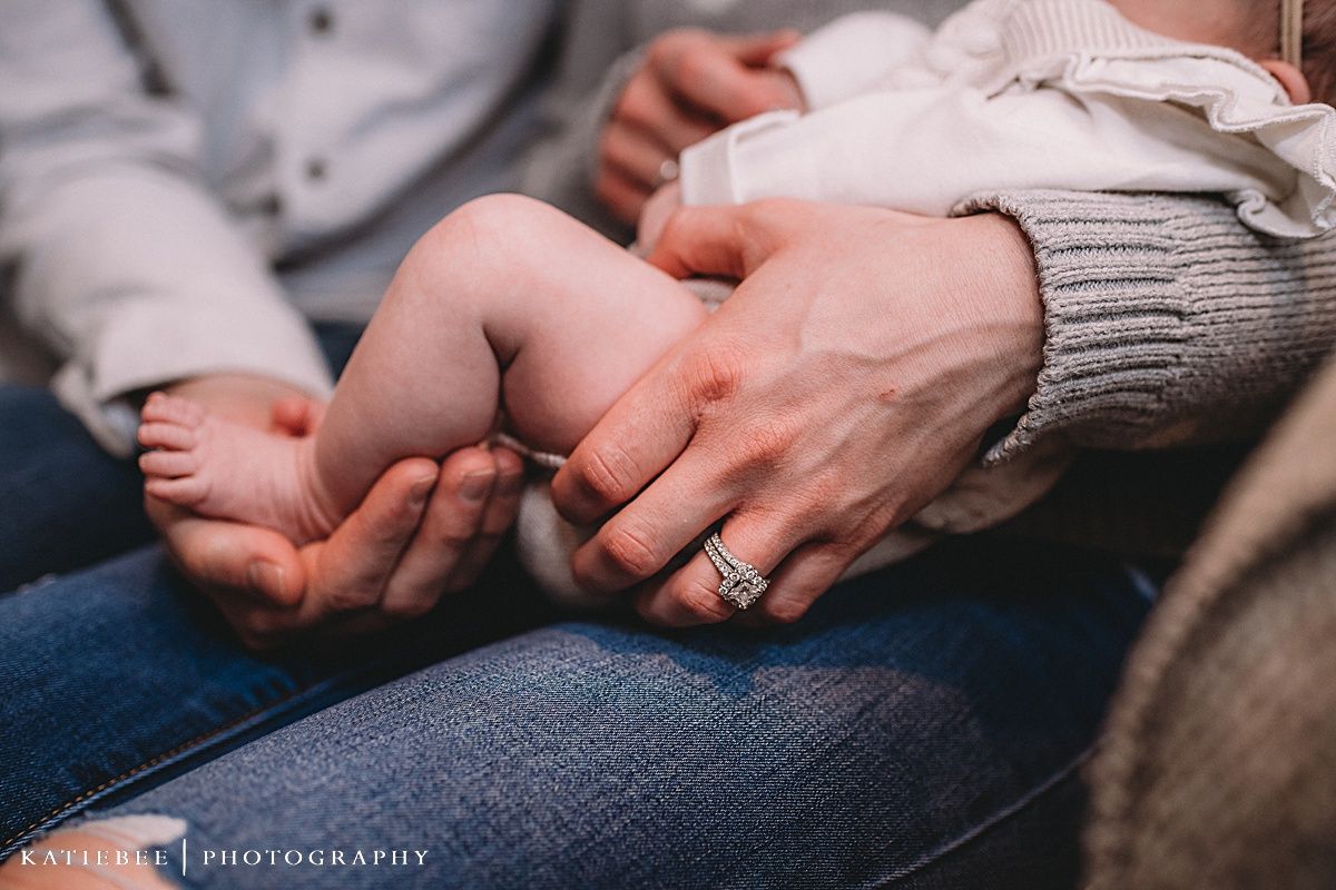 Close-up of tiny baby feet being gently held in adult hands with a wedding ring visible.