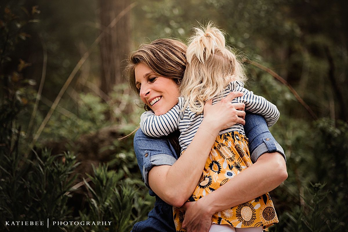 A candid emotional hug captured between two people in a wooded outdoor setting.