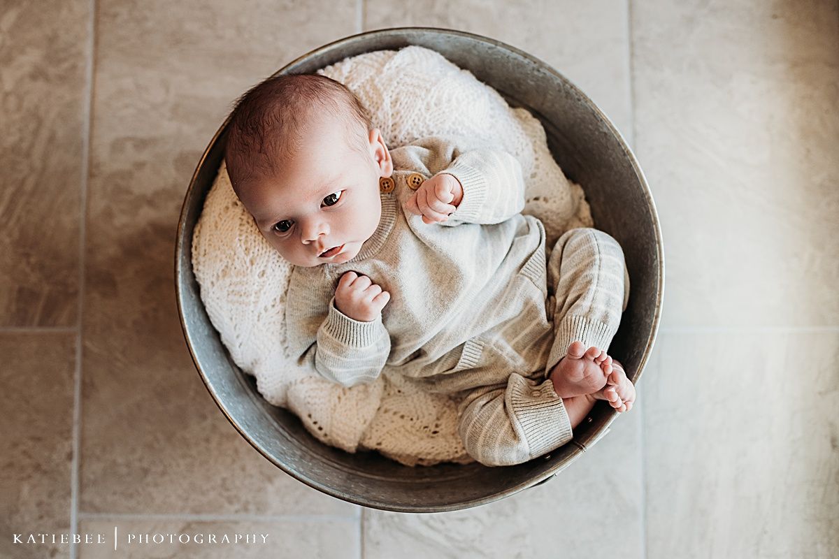 Infant wearing cream outfit nestled in circular metal basin.