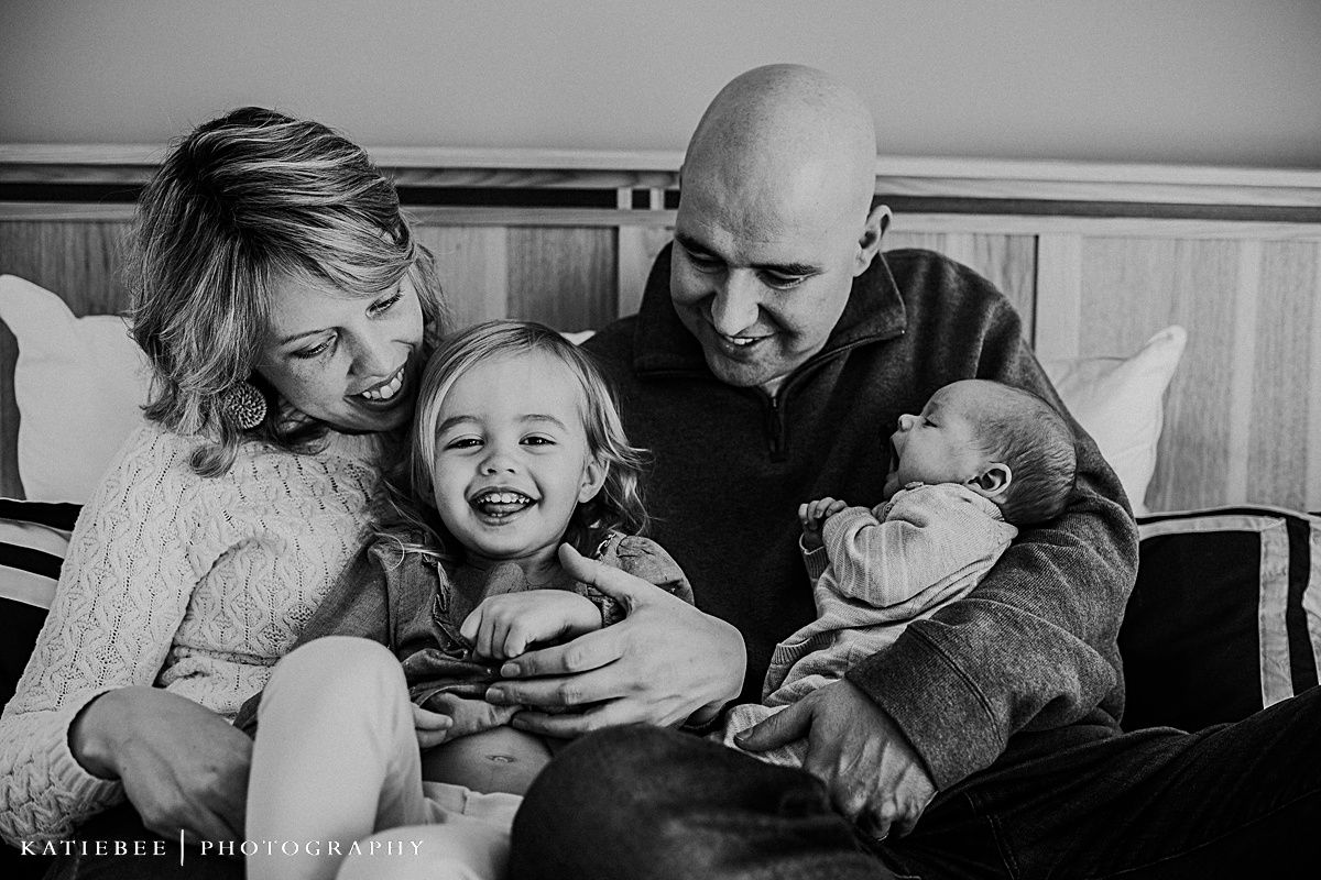 A black and white portrait of a family sharing laughs while sitting on their bed.