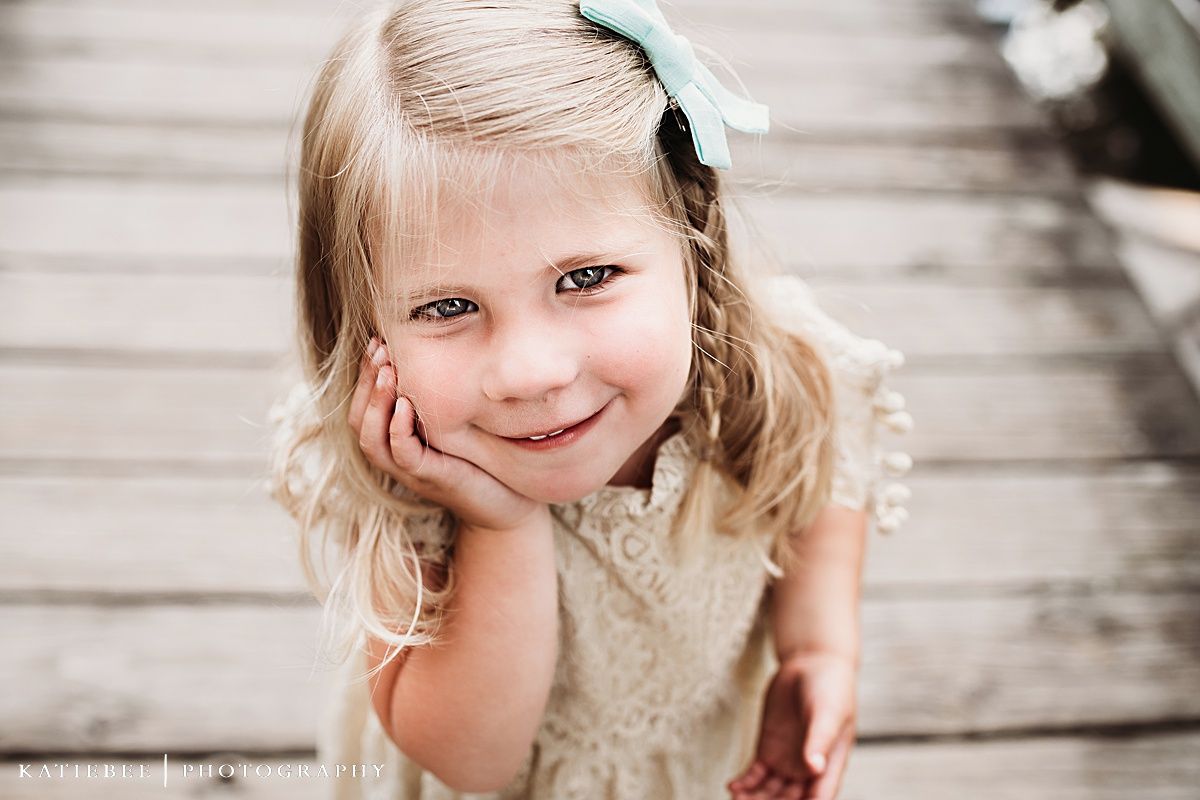 Portrait of young child with blue bow smiling on wooden deck.
