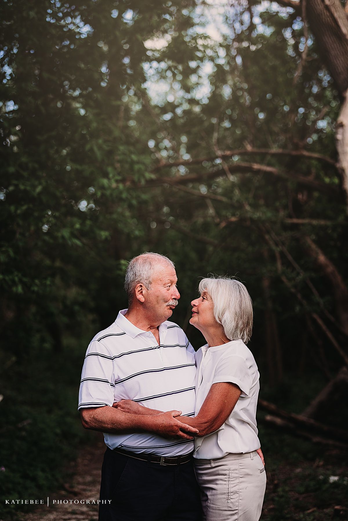 A loving senior couple embracing outdoors in a wooded setting.