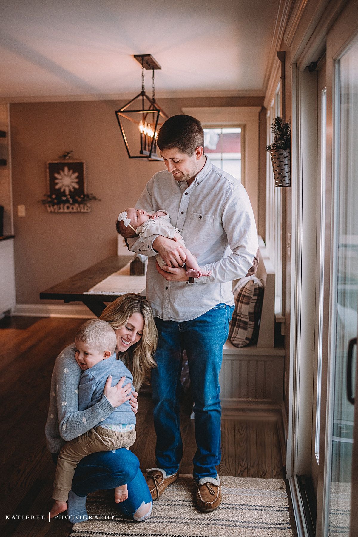 A loving family moment captured in a warm-toned home interior with rustic lantern lighting and large windows.