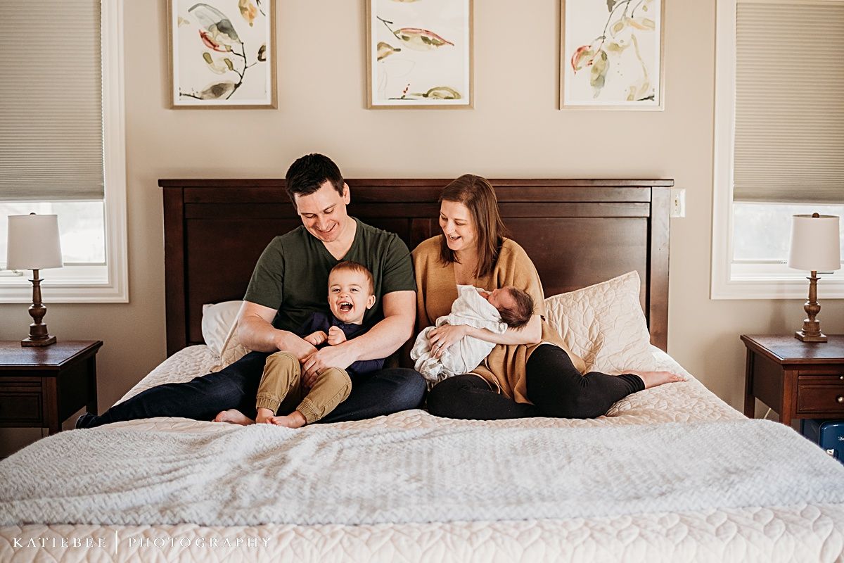 Family relaxing together on a bed with white bedding beneath decorative bird artwork.