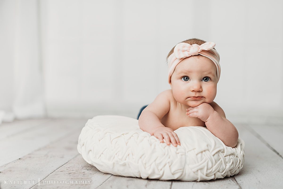 Baby on white quilted pillow wearing headband during minimalist photo shoot.