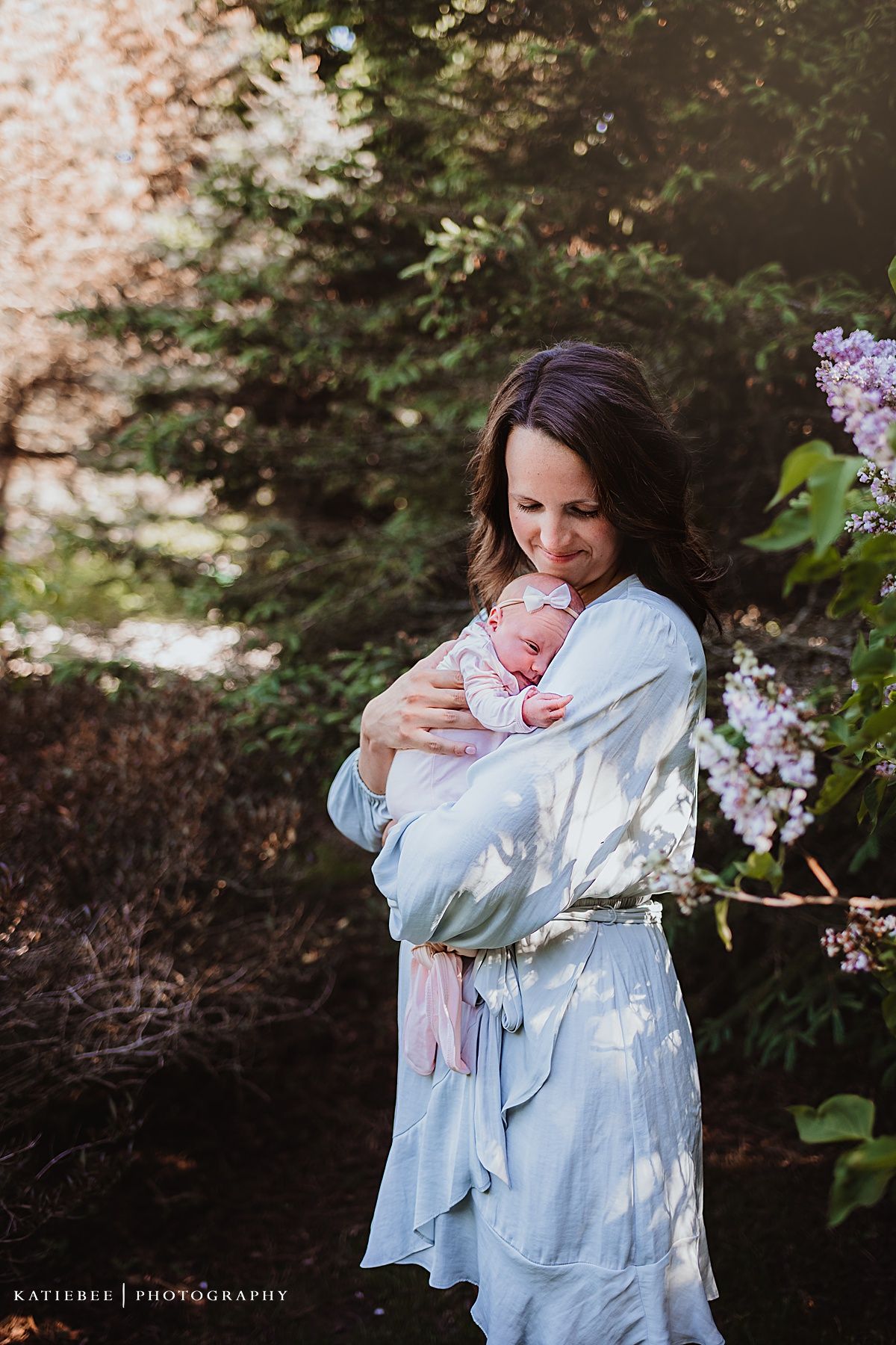 Gentle outdoor portrait with a sleeping infant against light blue clothing near blooming flowers.