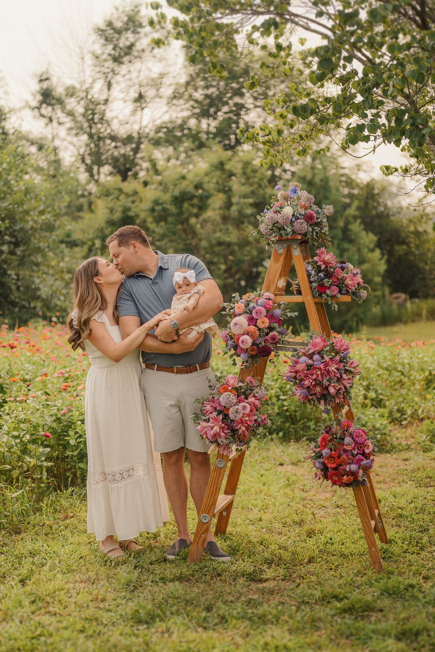 Couple shares intimate moment near wooden easel decorated with vibrant pink and purple flowers in outdoor garden.