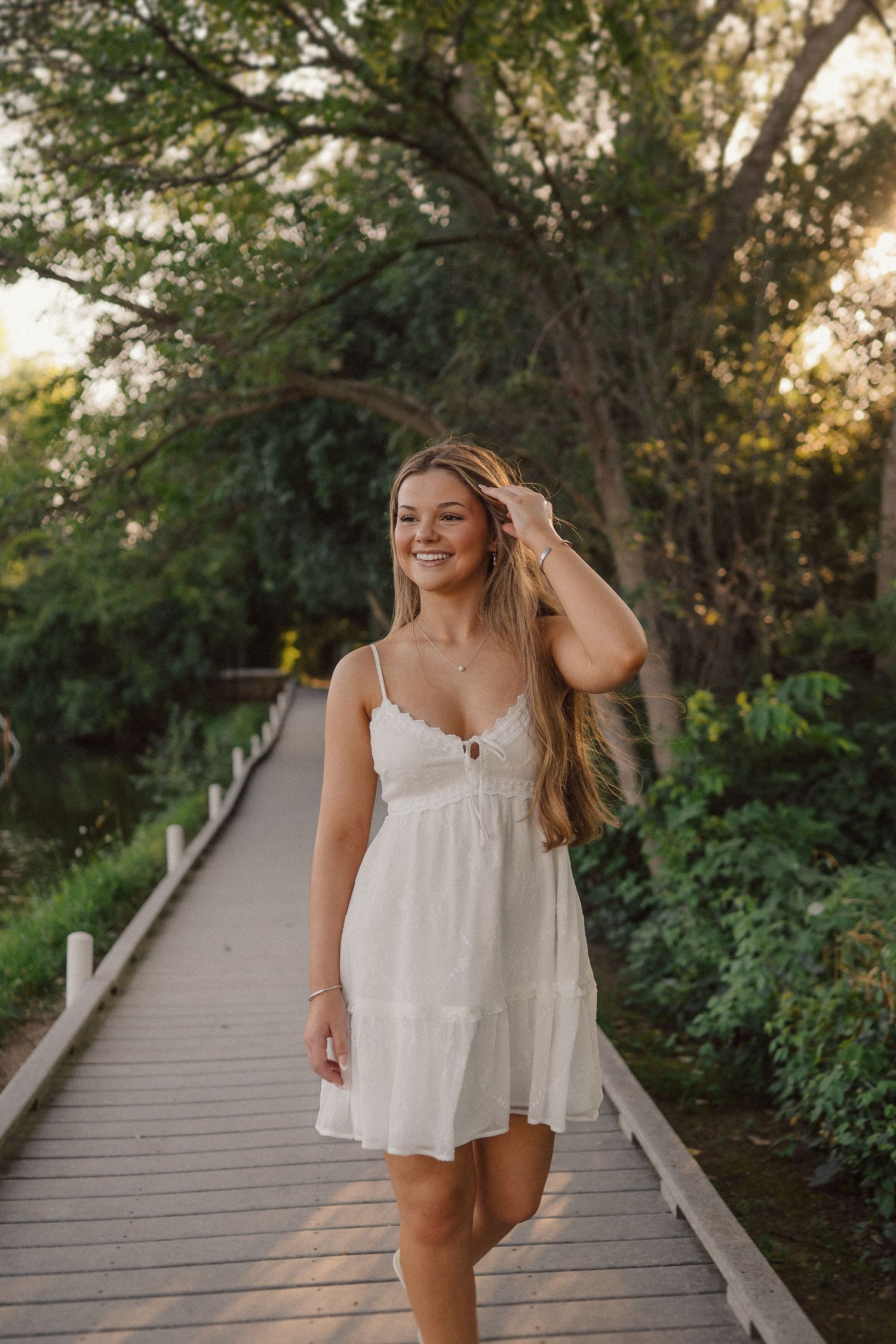 Summer portrait session on a wooden boardwalk surrounded by lush greenery at sunset.