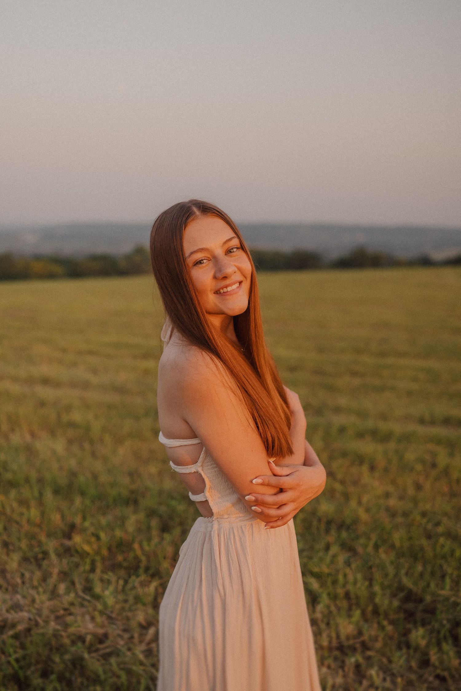 A person in a white dress poses playfully in a golden field at sunset.