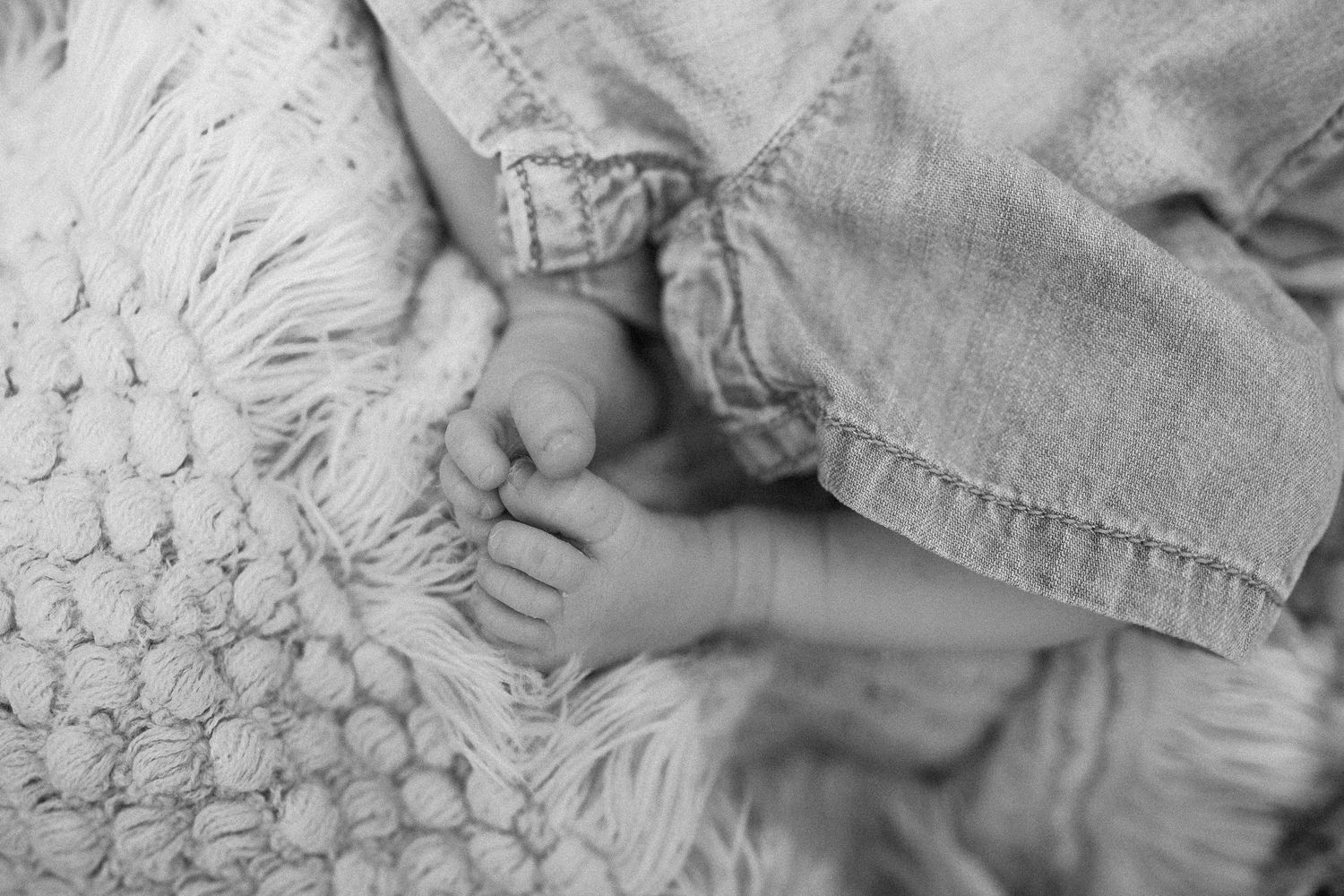 A baby's feet rest gently on a textured knit blanket while wearing denim clothing.