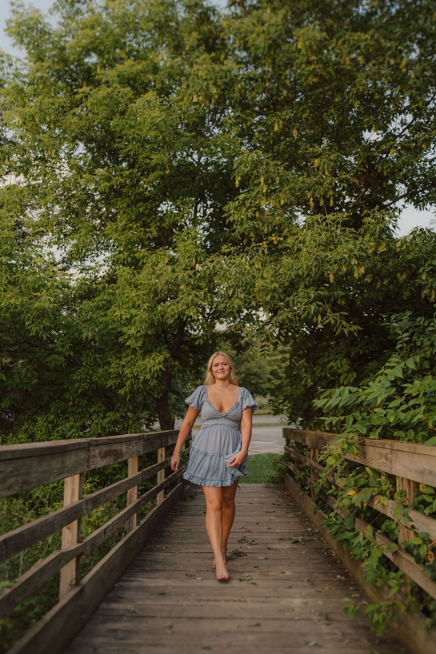 Someone in a blue dress walks along a wooden boardwalk path surrounded by lush summer greenery.