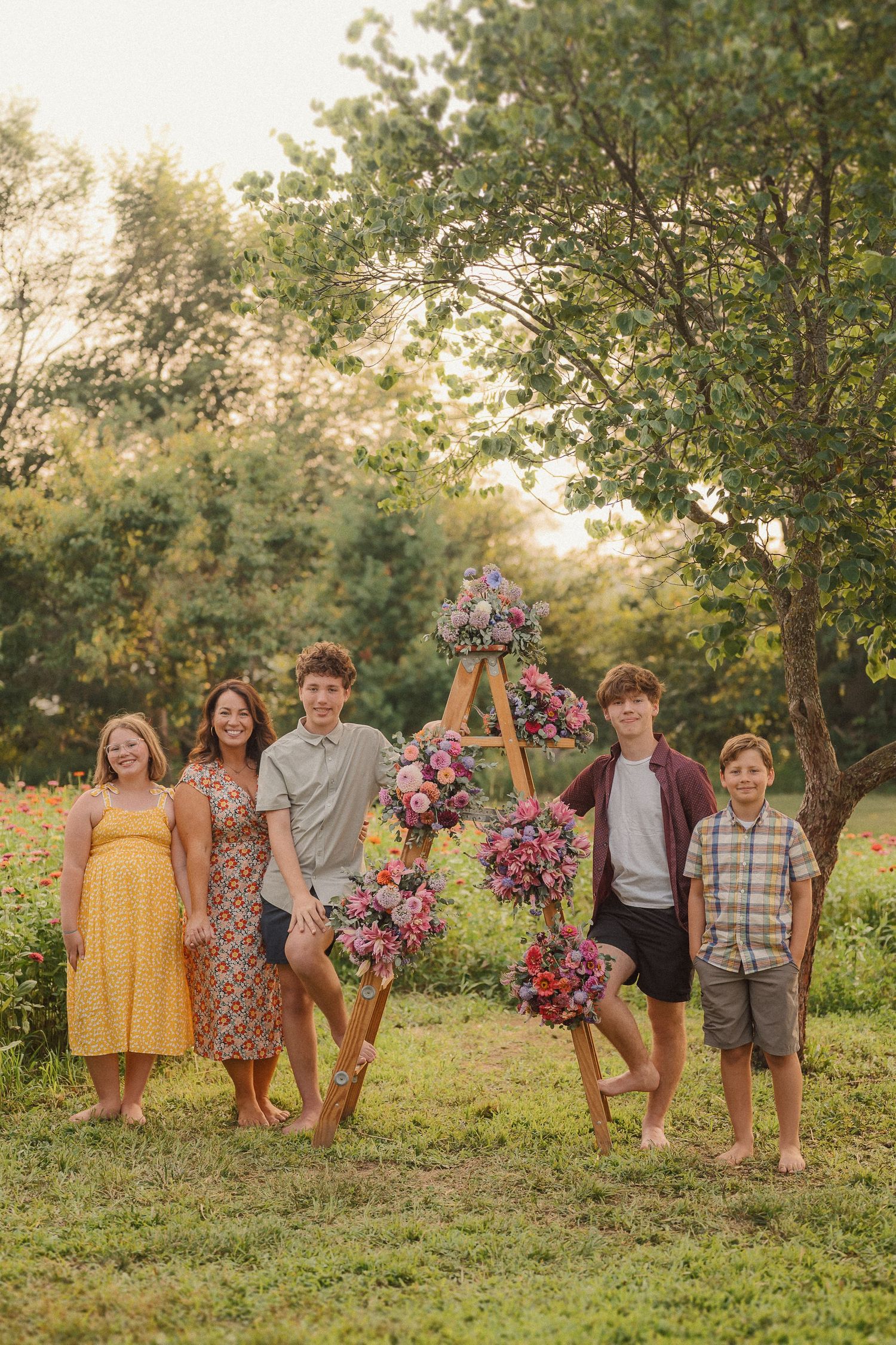 Group gathered around wooden ladder decorated with pink floral arrangements in outdoor garden setting.