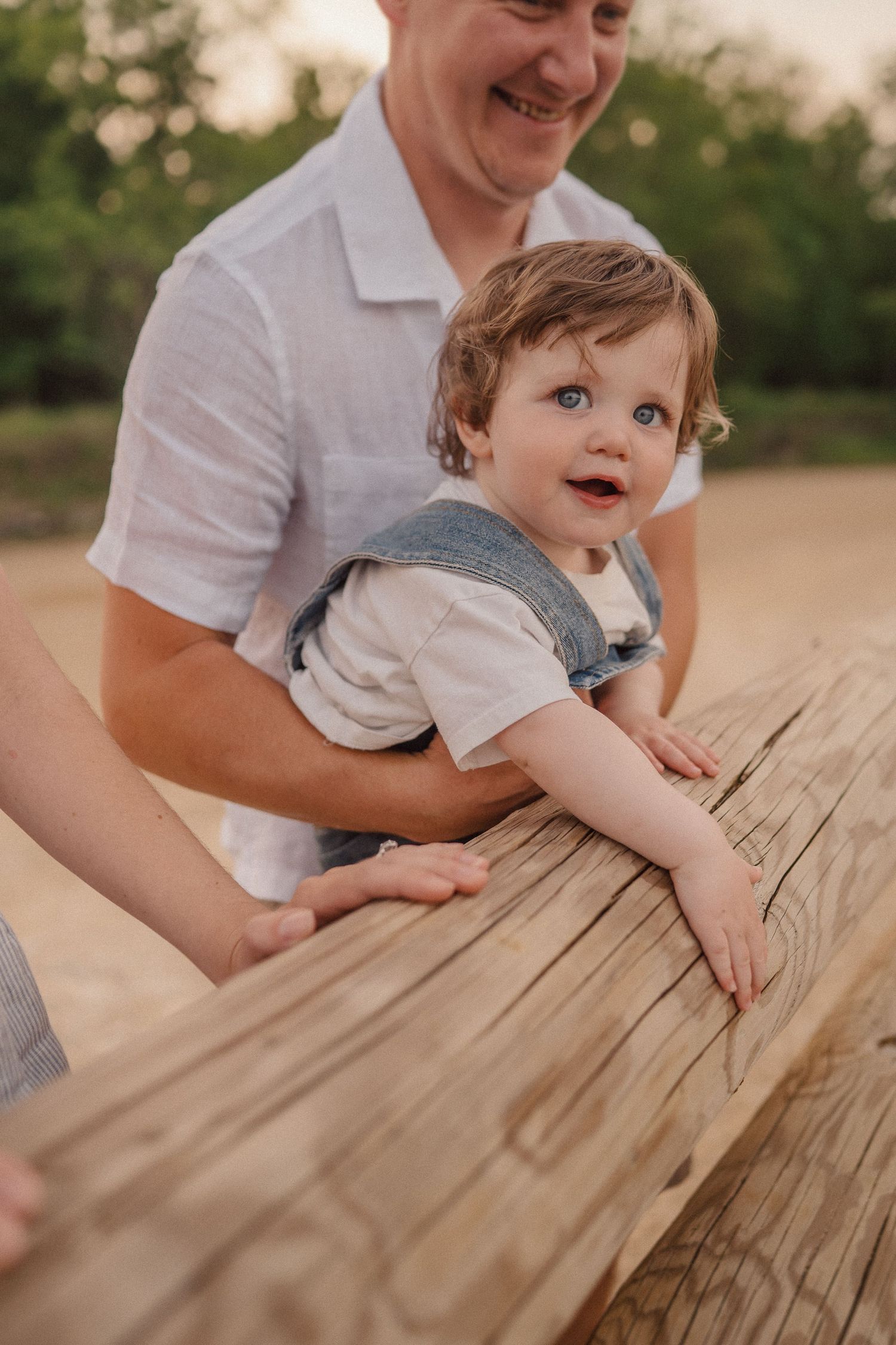 A joyful moment captured as a child leans on a wooden surface while being supported from behind.