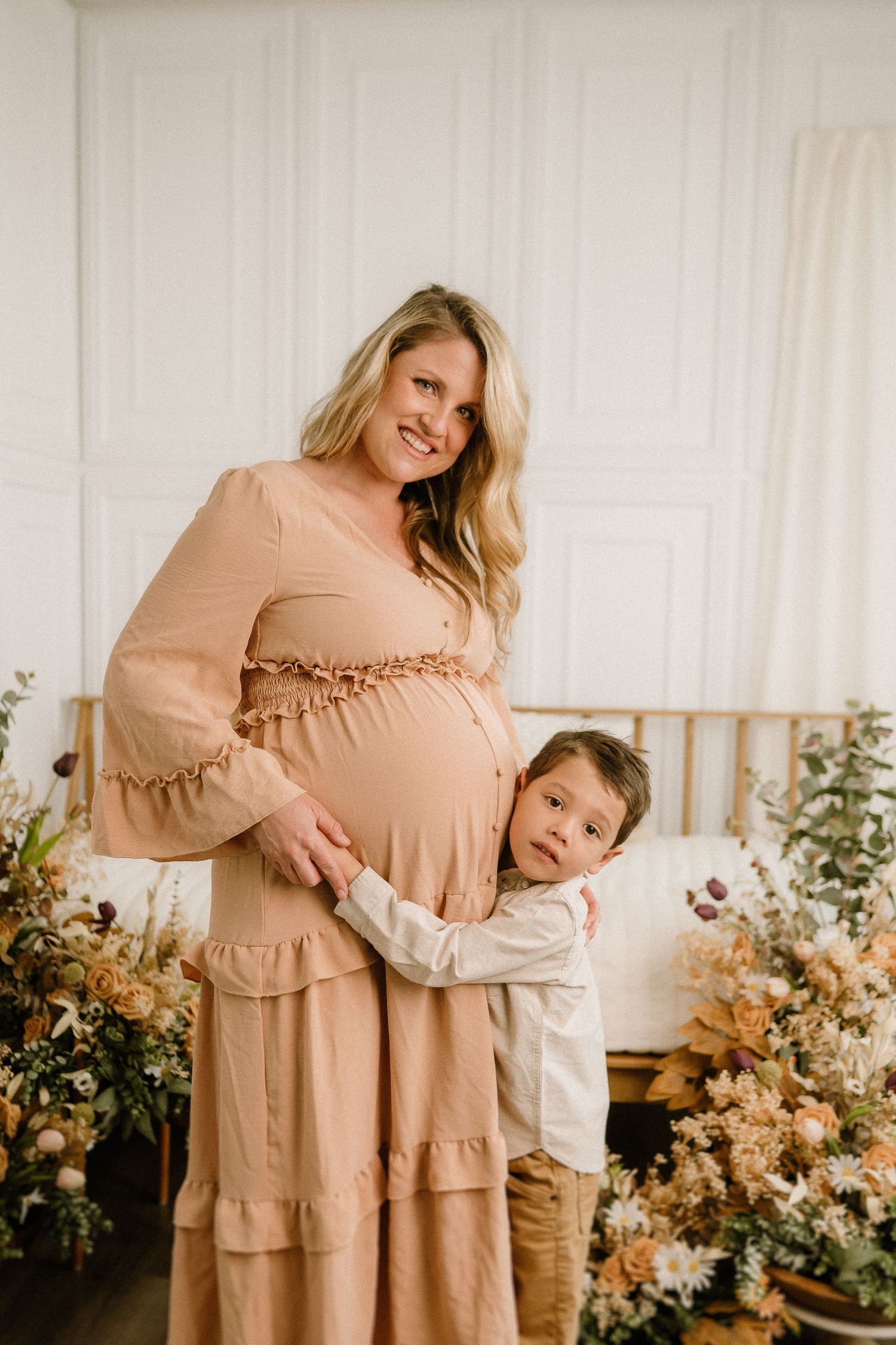 Intimate portrait session with flowing peach dress and floral arrangements in a bright white studio setting.