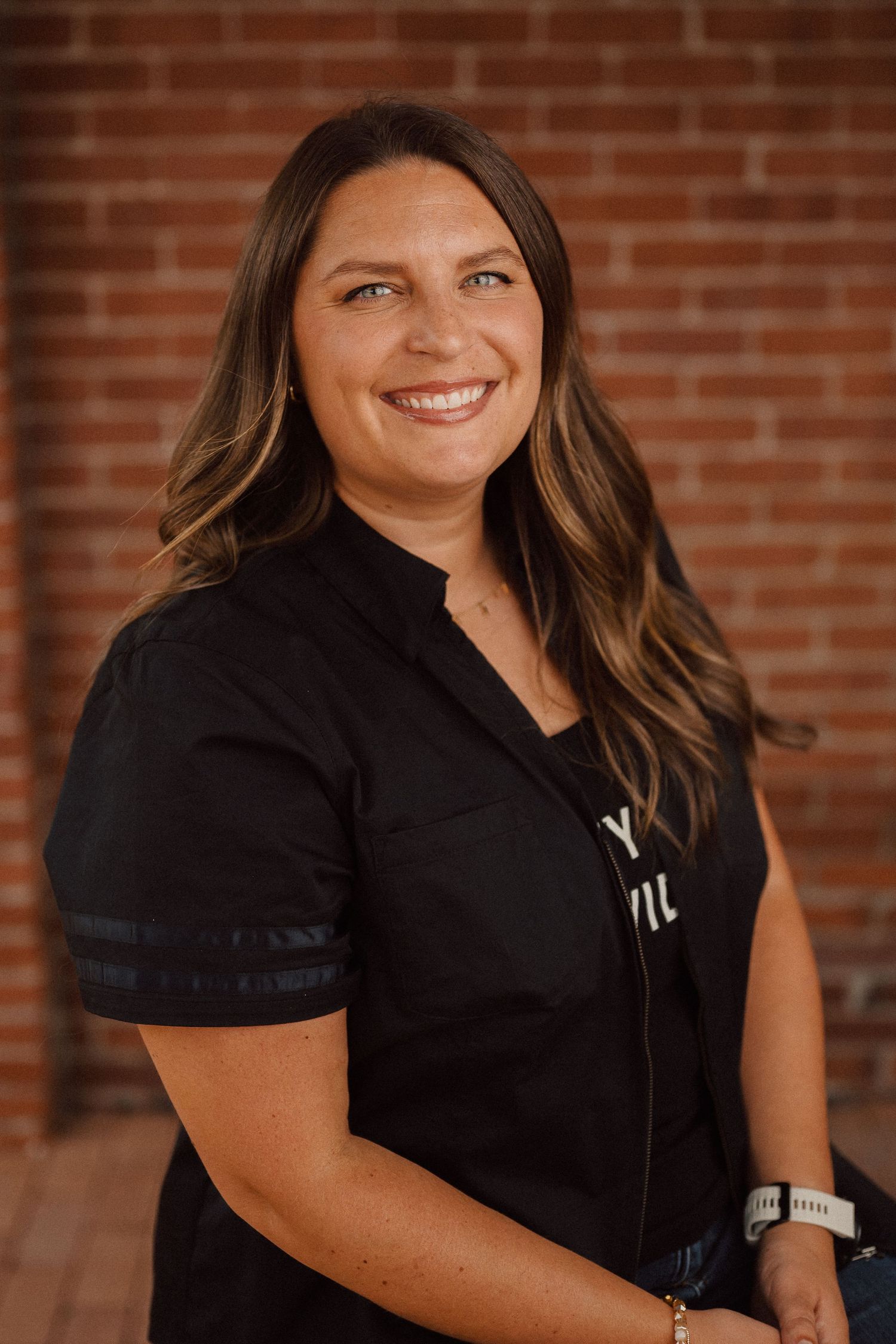 Professional headshots against a brick wall showing a person in a black top with soft lighting and warm tones.
