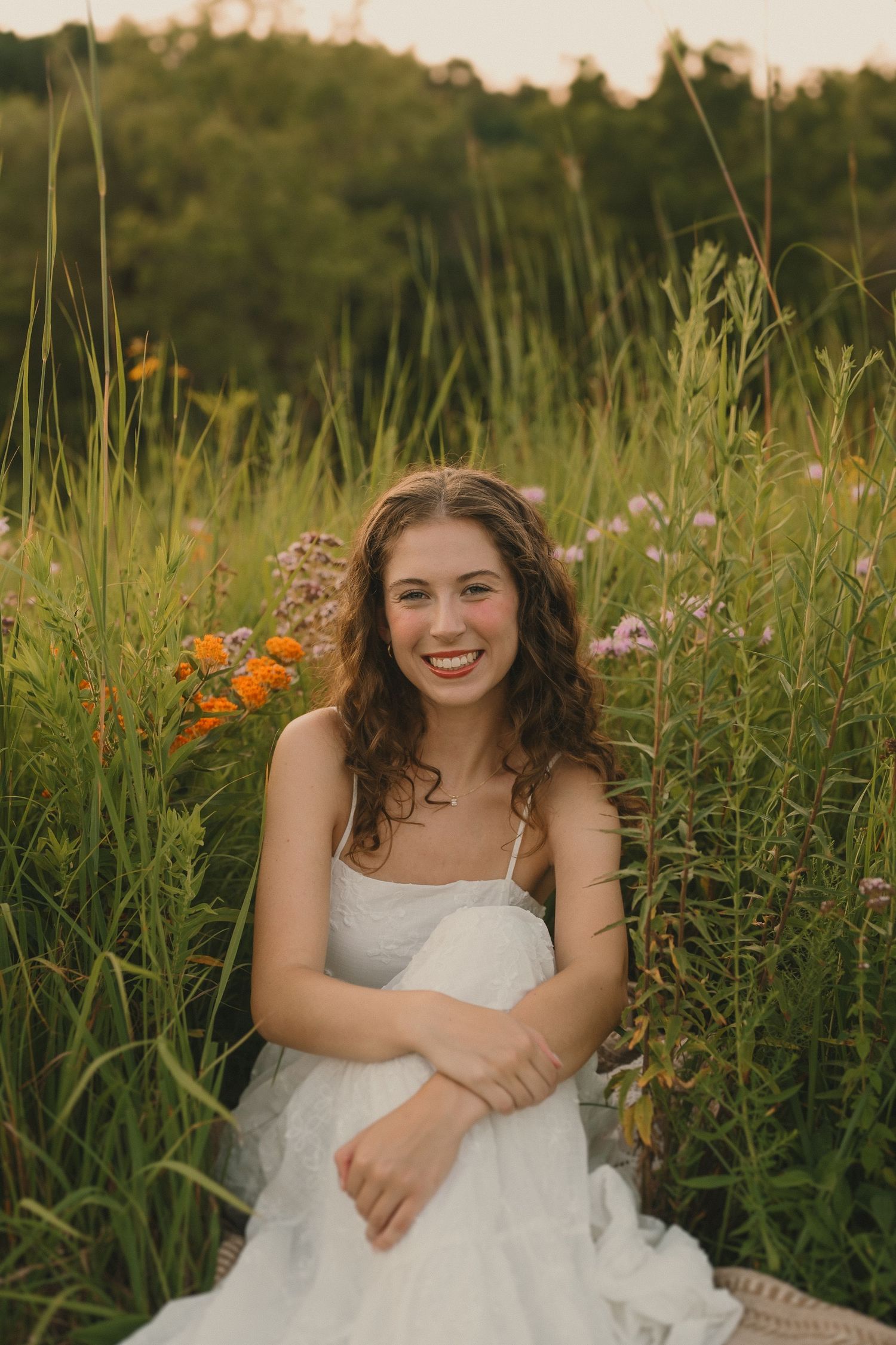 A white dress stands out against tall wildflowers and grasses in a summer meadow during golden hour.