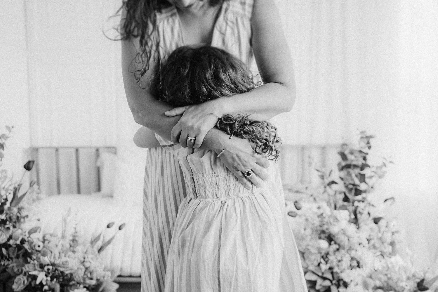 Black and white photo showing someone in a flowy dress holding a small dark-colored dog against their chest.