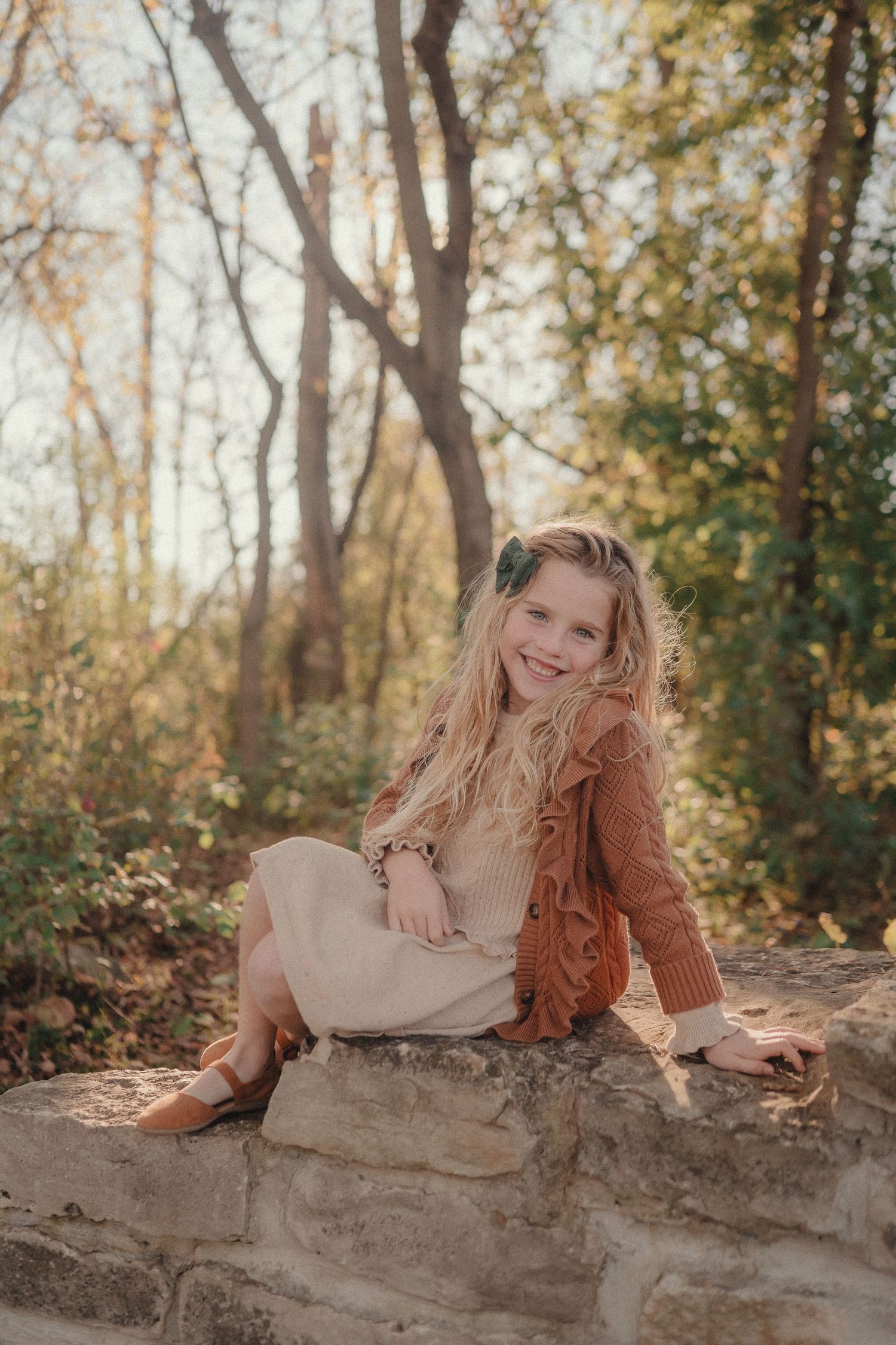 Person in rust-colored sweater reclining on stone wall during autumn outdoor portrait session.