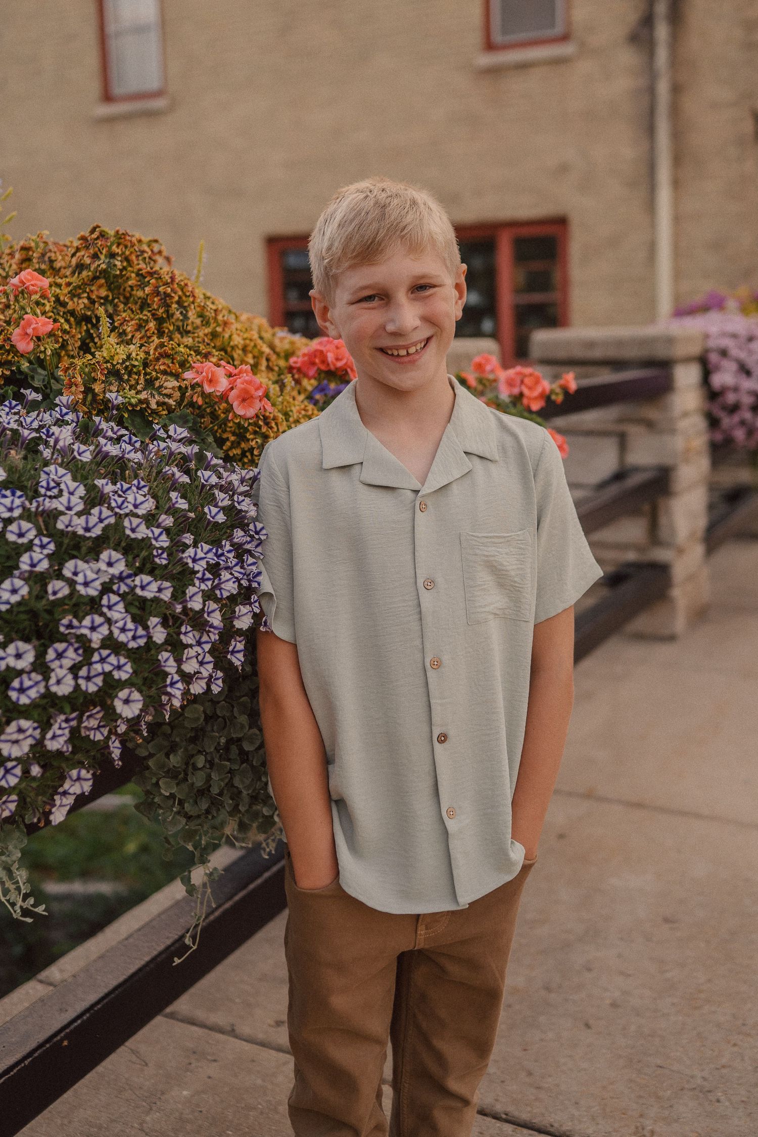 Child in casual attire posing near colorful flower planters along a brick pathway.