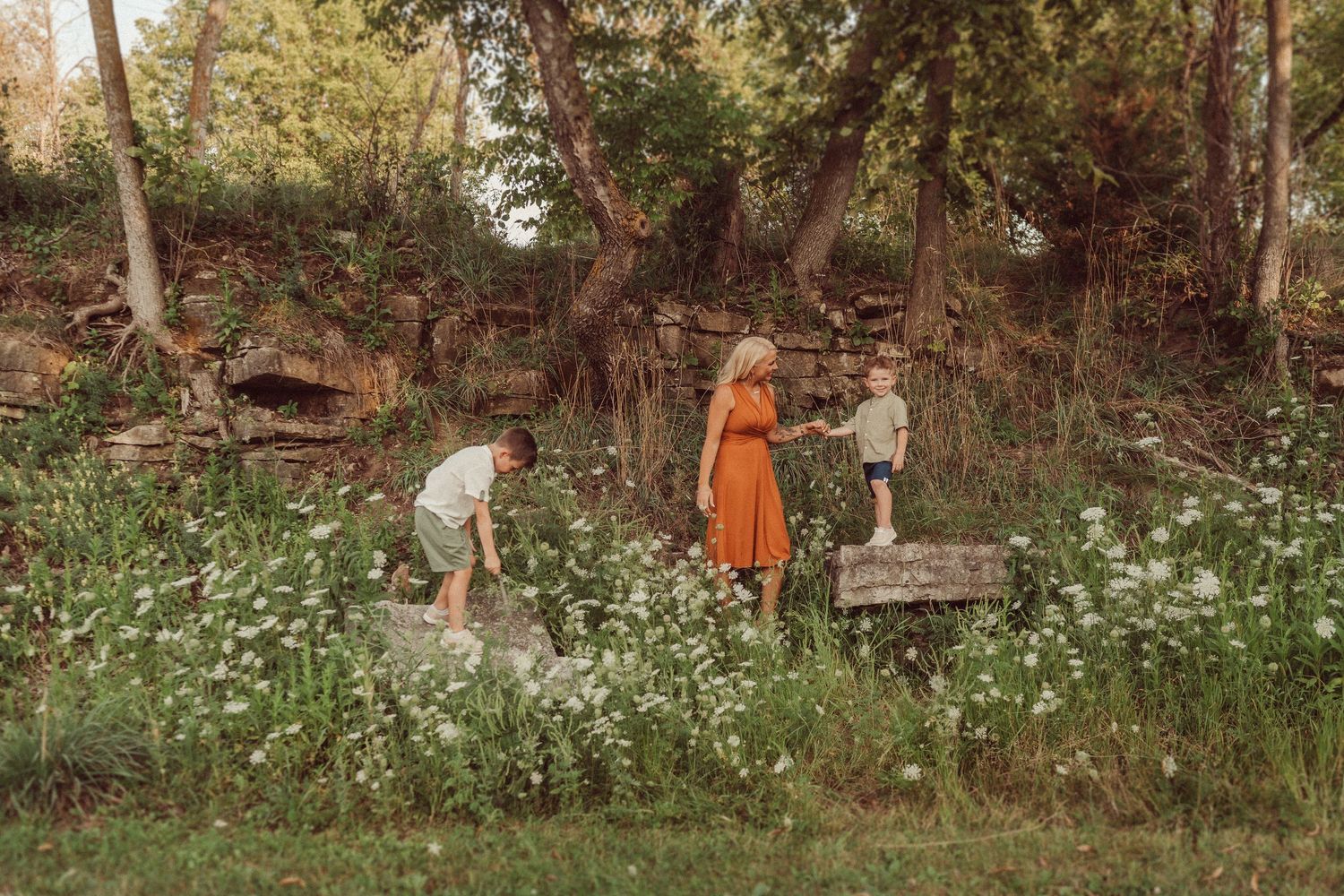 People exploring stone wall area surrounded by white wildflowers in wooded setting.