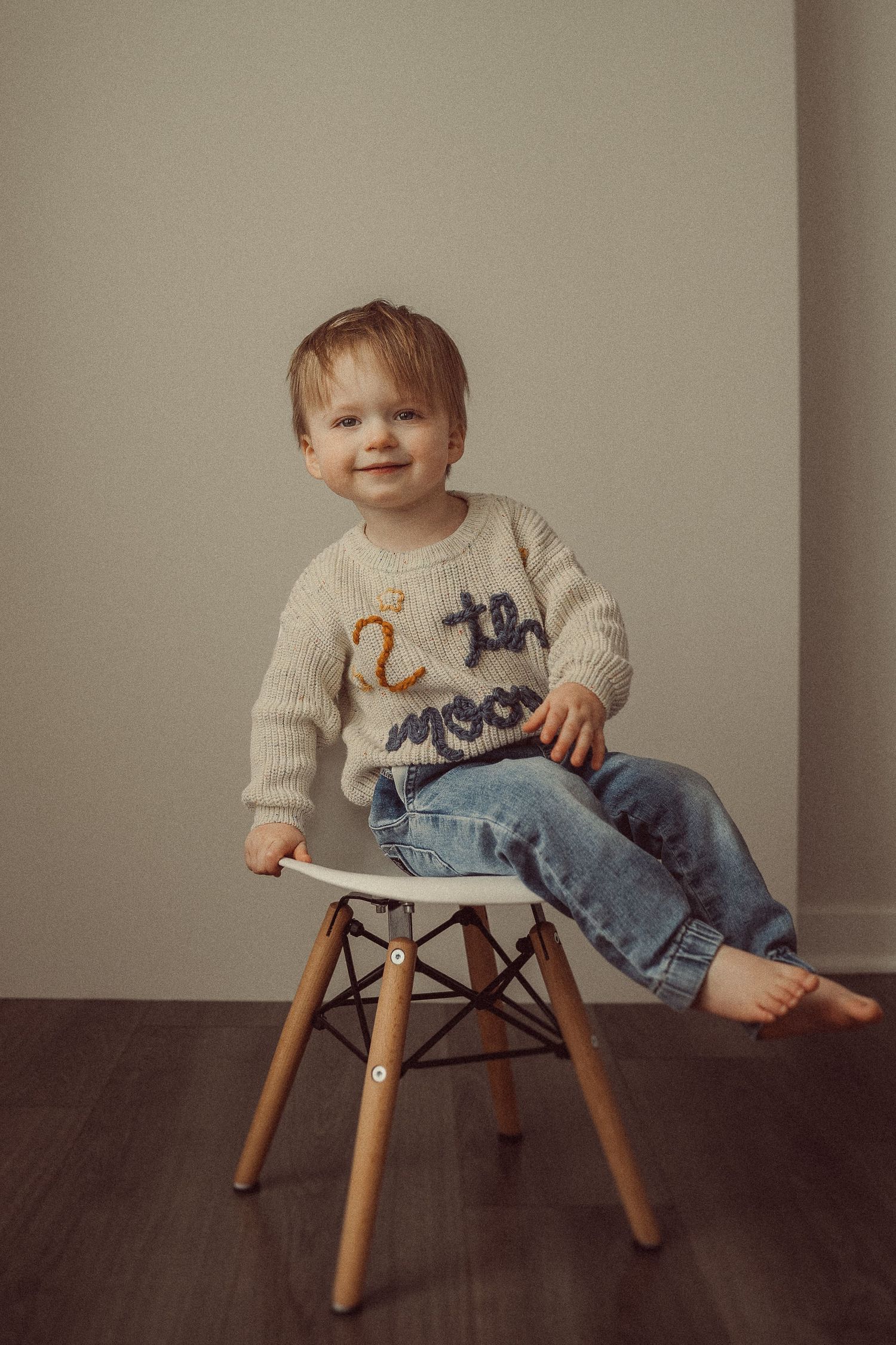 Child seated comfortably on Eames-style chair wearing cream sweater and jeans.