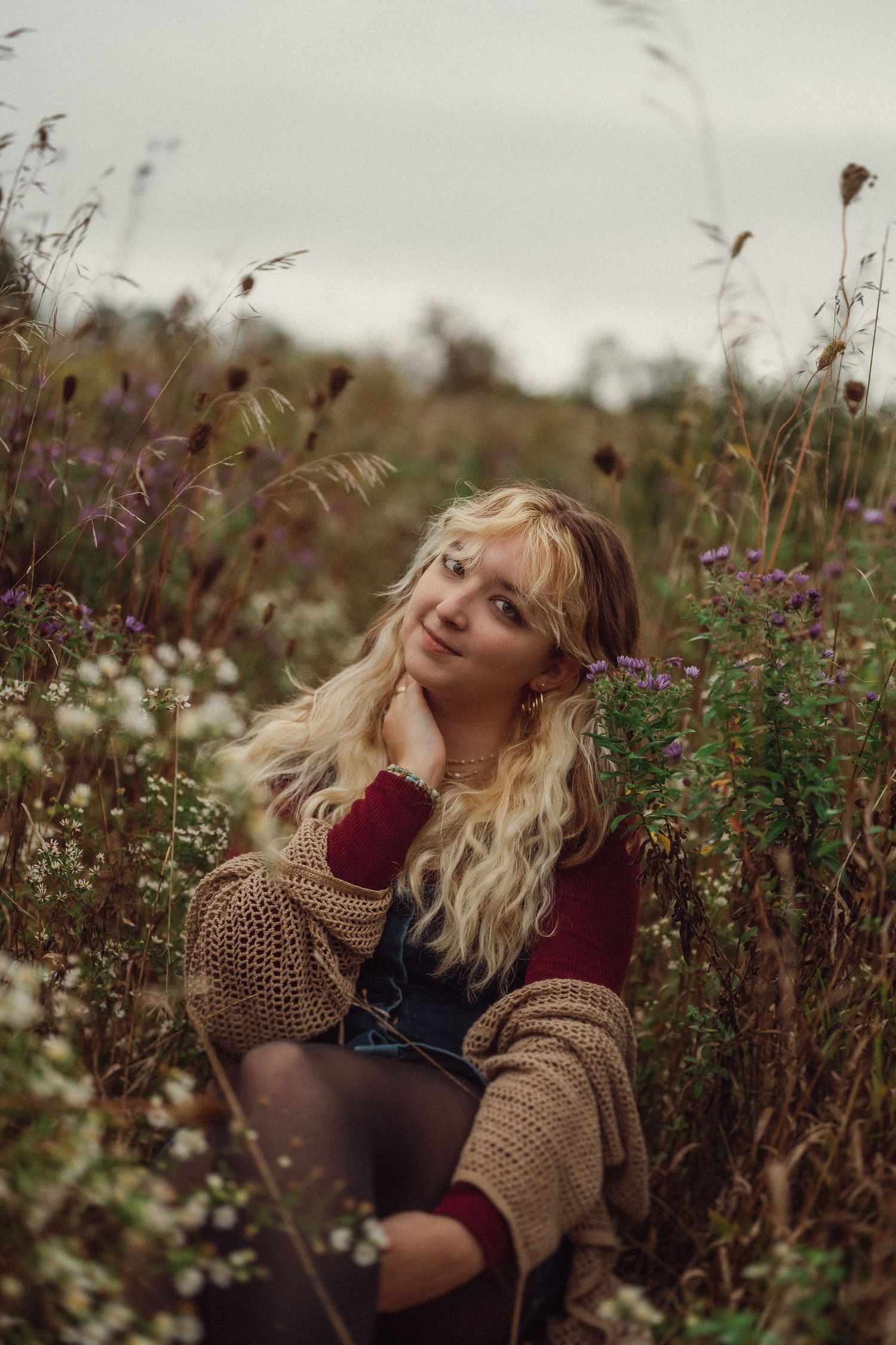 Rustic autumn portrait in overalls and sweater among wild meadow flowers.