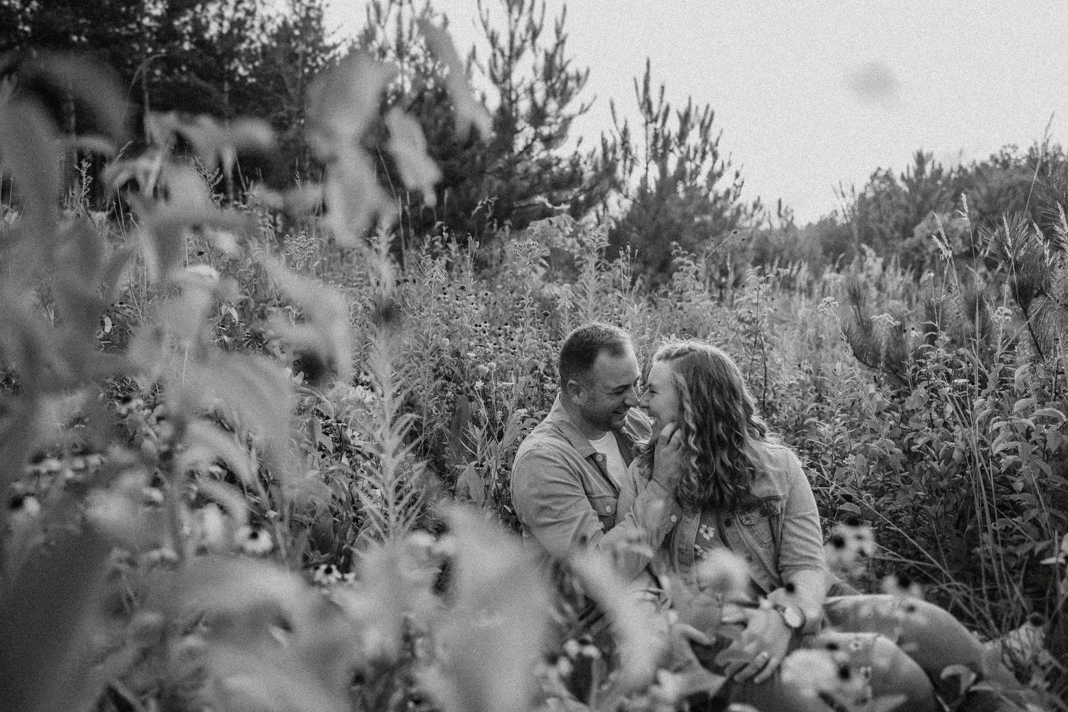 A romantic black and white portrait of a couple nestled in tall grass and wildflowers.