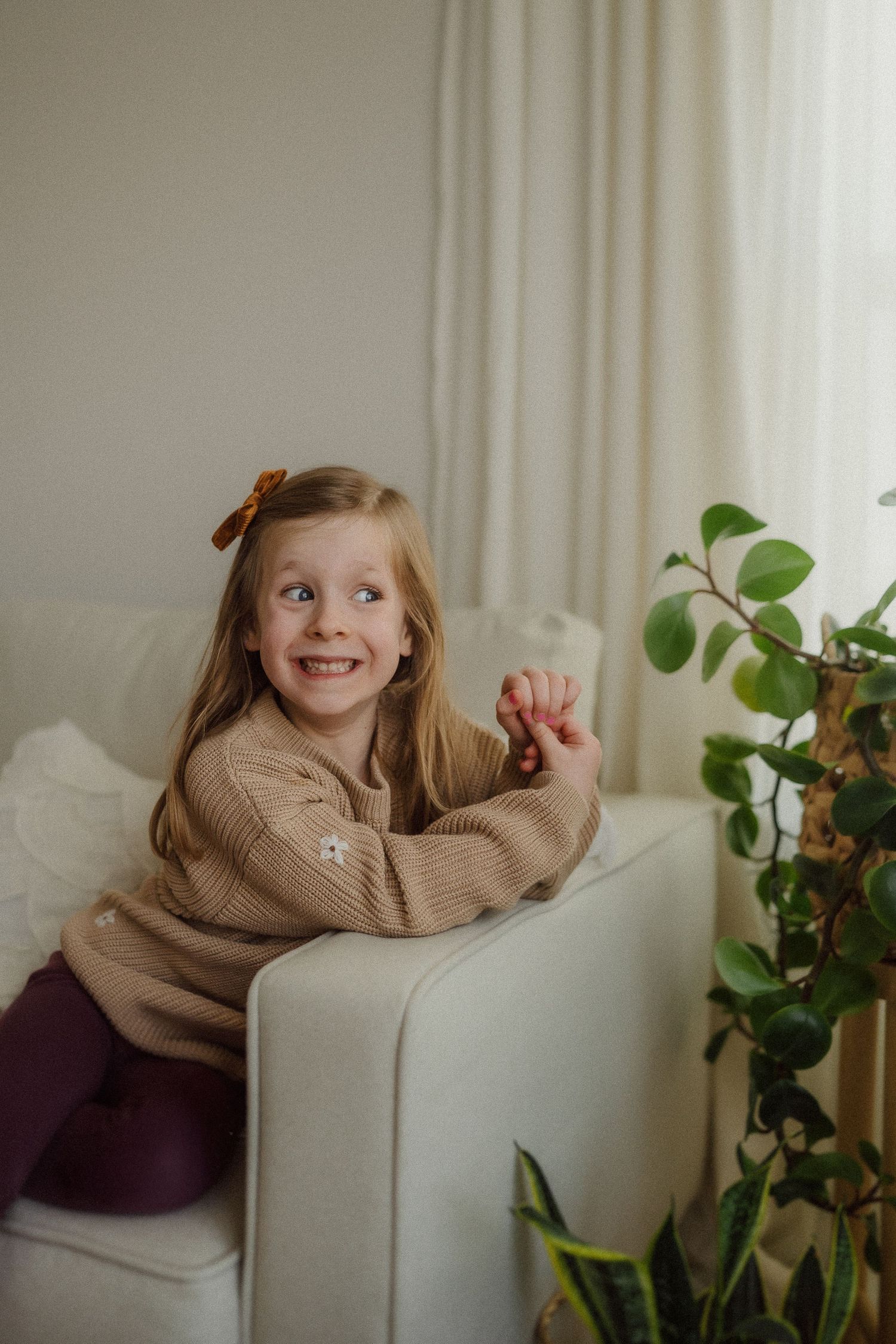 Joyful moment captured on white sofa with child in tan sweater making silly expressions.