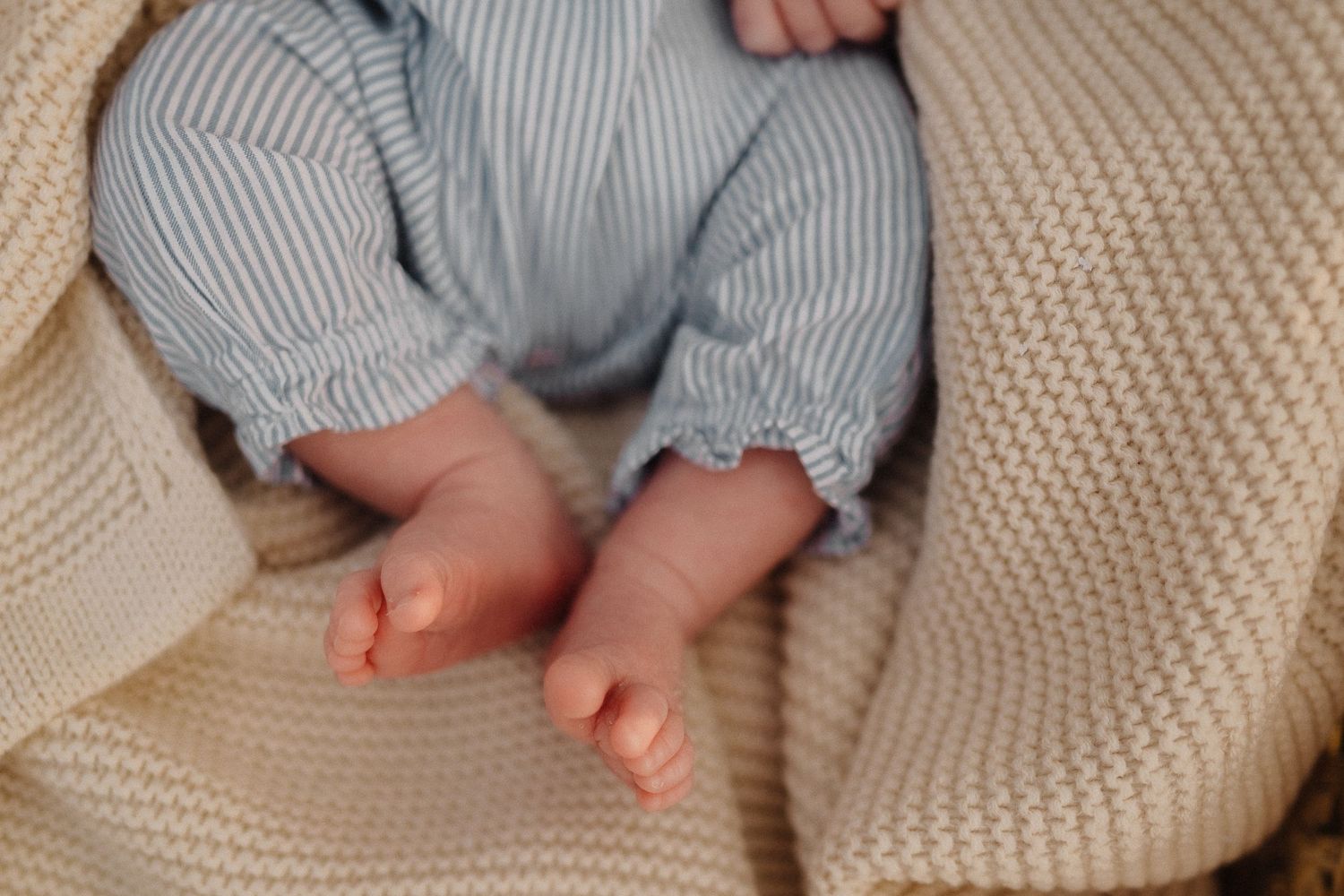 Close-up of tiny baby feet wearing blue striped pants against cream knit blanket.