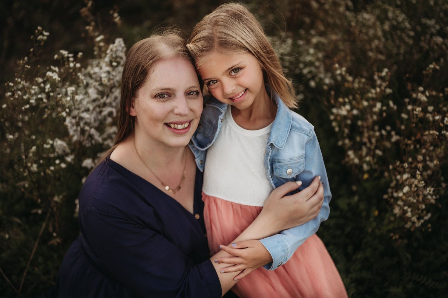 Two people share a warm embrace while smiling outdoors against a natural background in golden light.