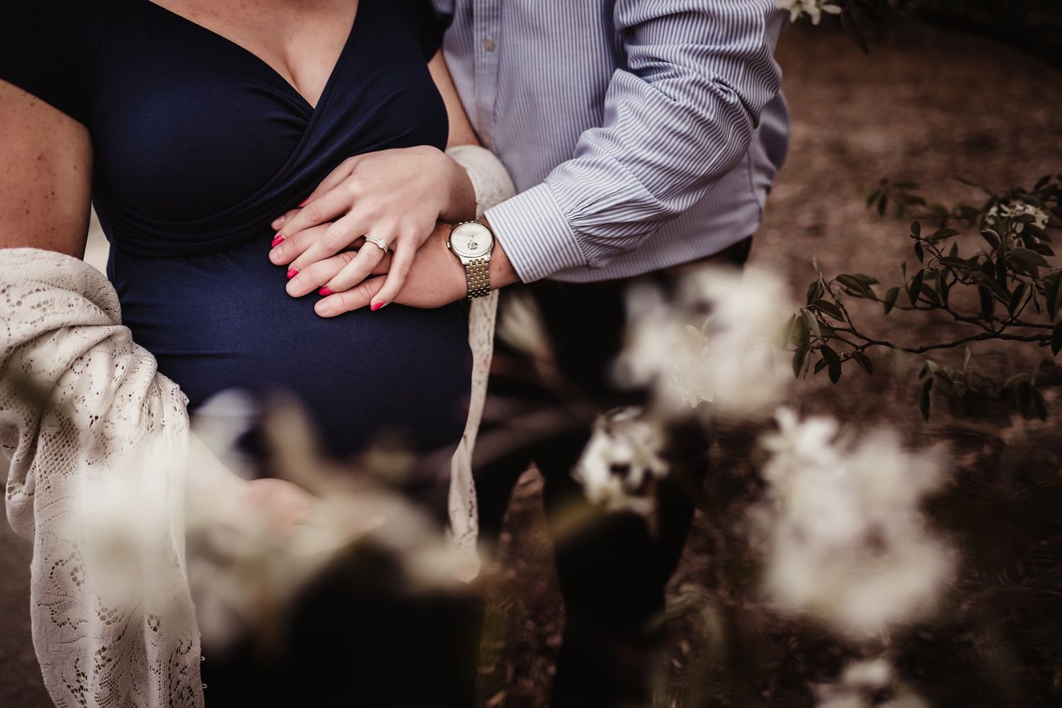 Close-up of hands tenderly resting on maternity bump with lace shawl detail.