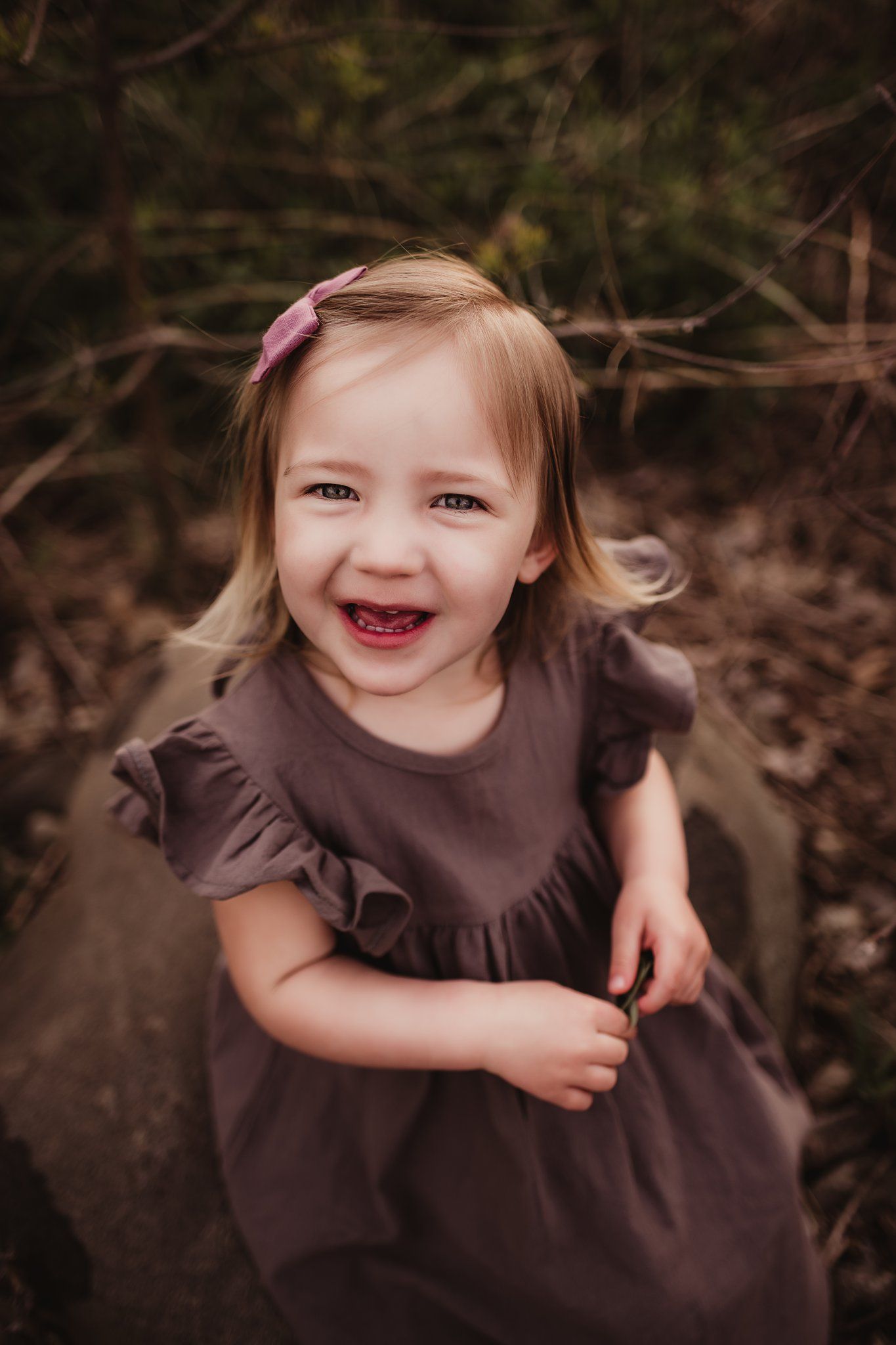 Child in brown dress smiling brightly during outdoor portrait session.