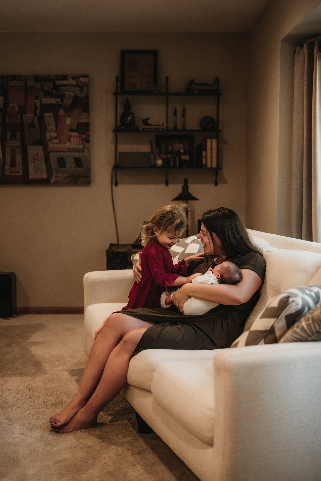 A family relaxes together on a white couch in a cozy living room with wall shelving.