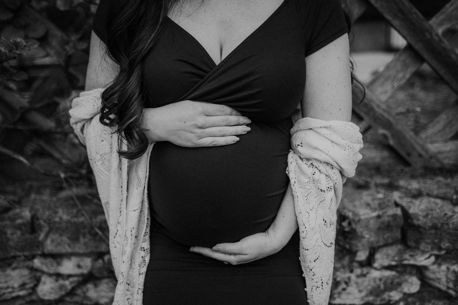 Black and white maternity photo showing hands cradling baby bump against stone wall.