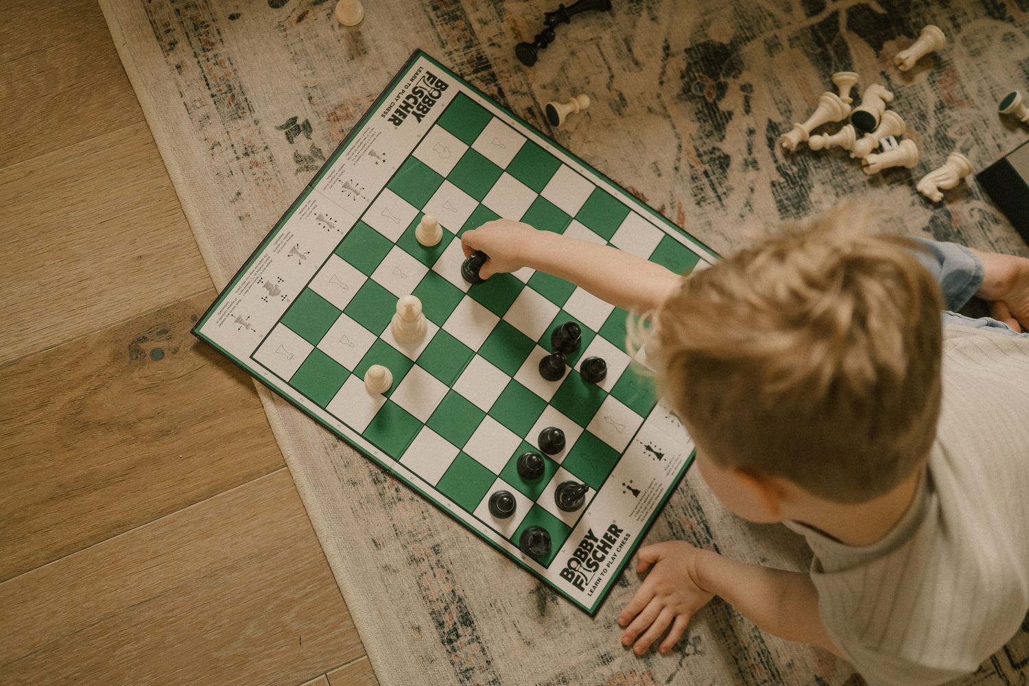 Young boy playing chess alone on floor viewed from above.