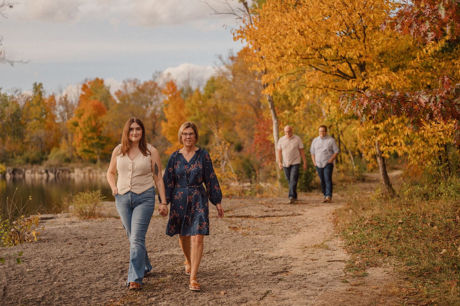 People walking on a dirt path surrounded by vibrant autumn trees with golden foliage during sunset.