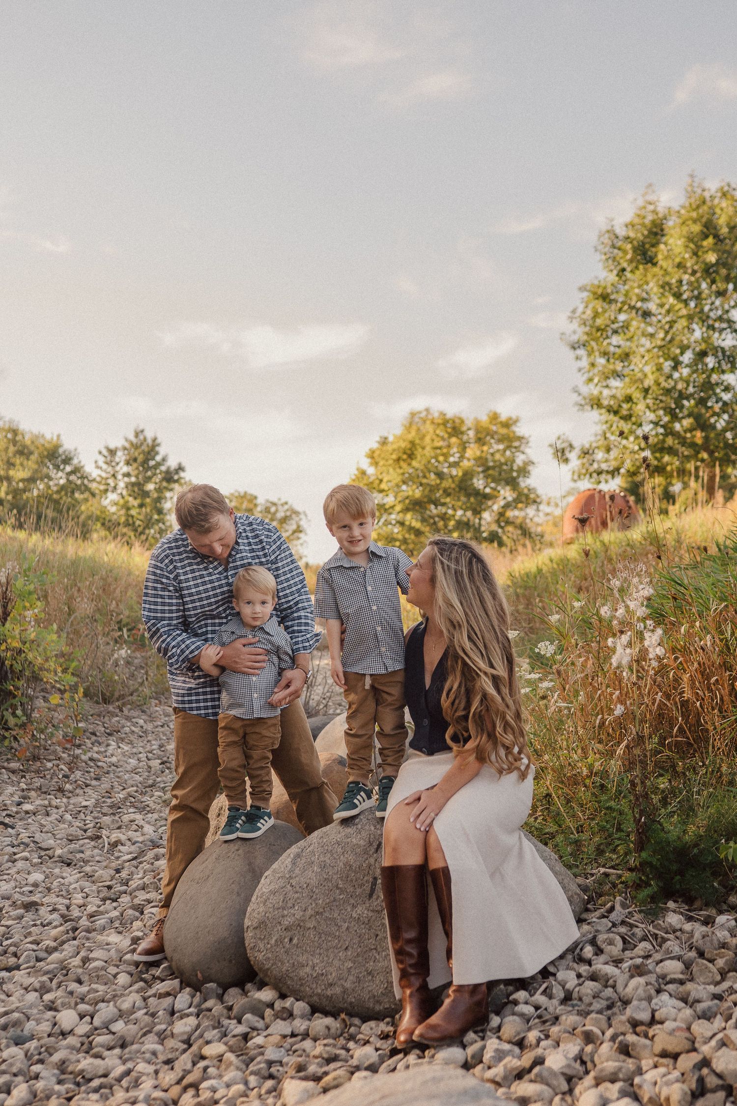 A family shares a tender moment together while sitting on large rocks at sunset in a natural outdoor setting.
