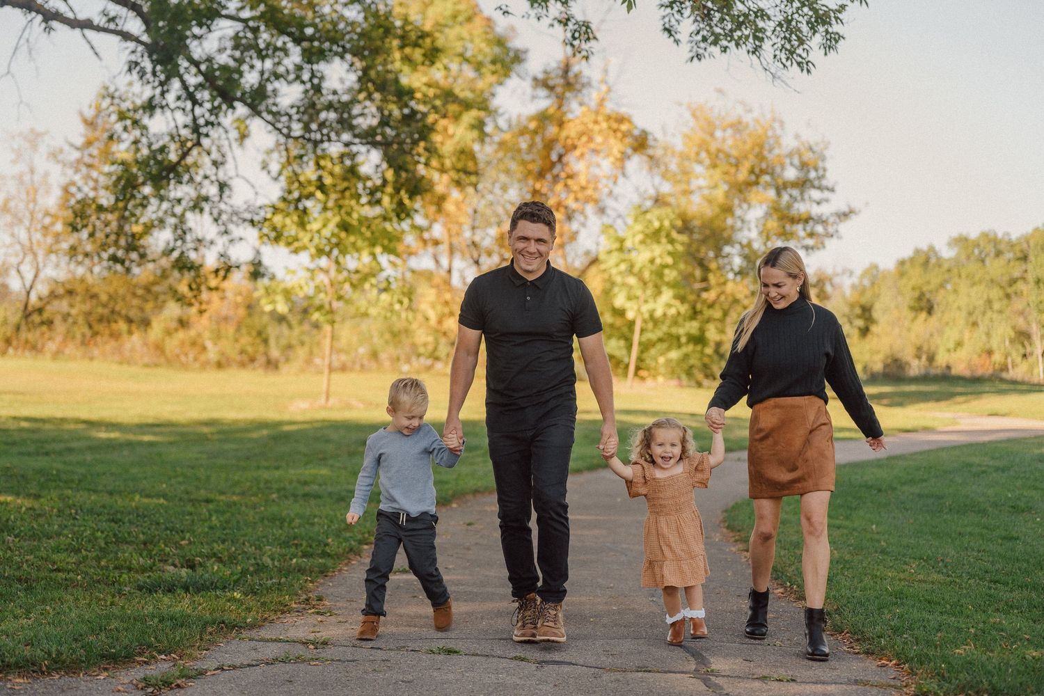 Family members walking together on a path through a grassy field during golden hour sunset.