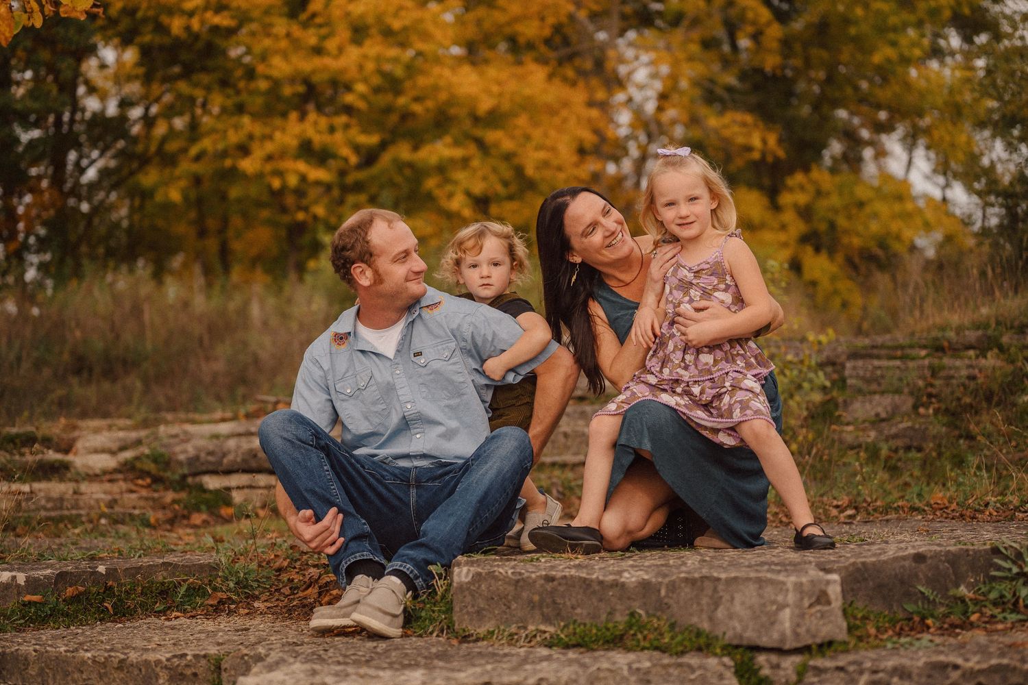 A family sits together on stone steps surrounded by vibrant autumn foliage during a fall photo session.