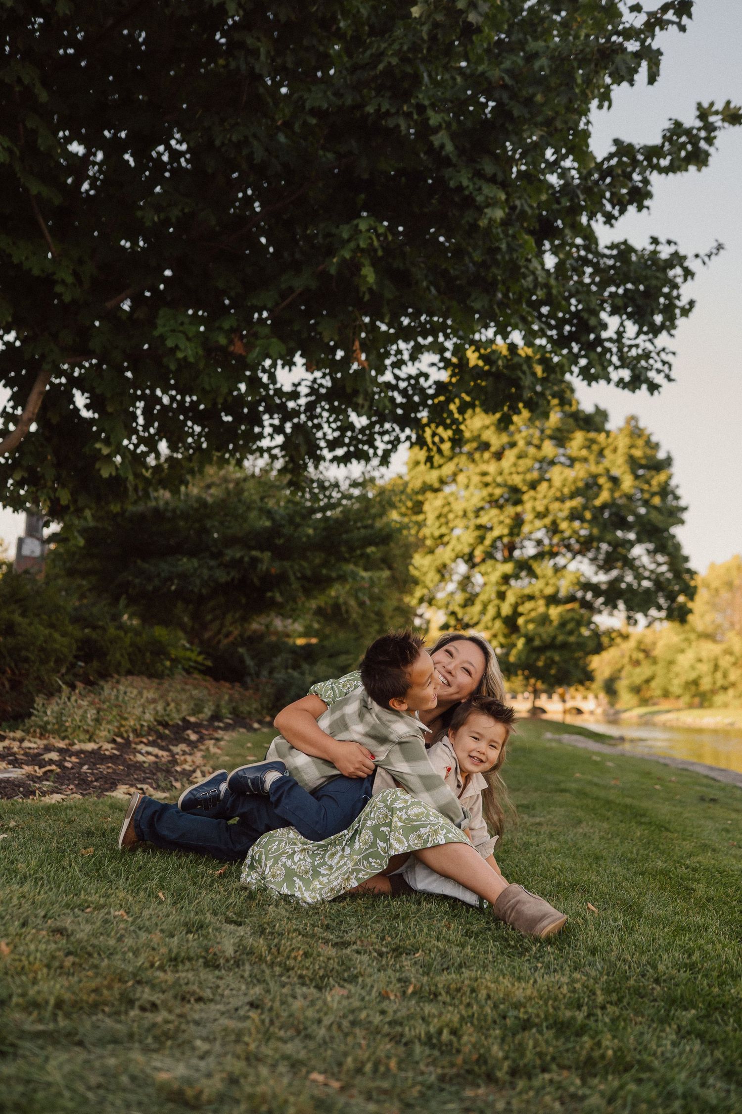 Intimate family moment captured while lying on grass under trees at sunset.