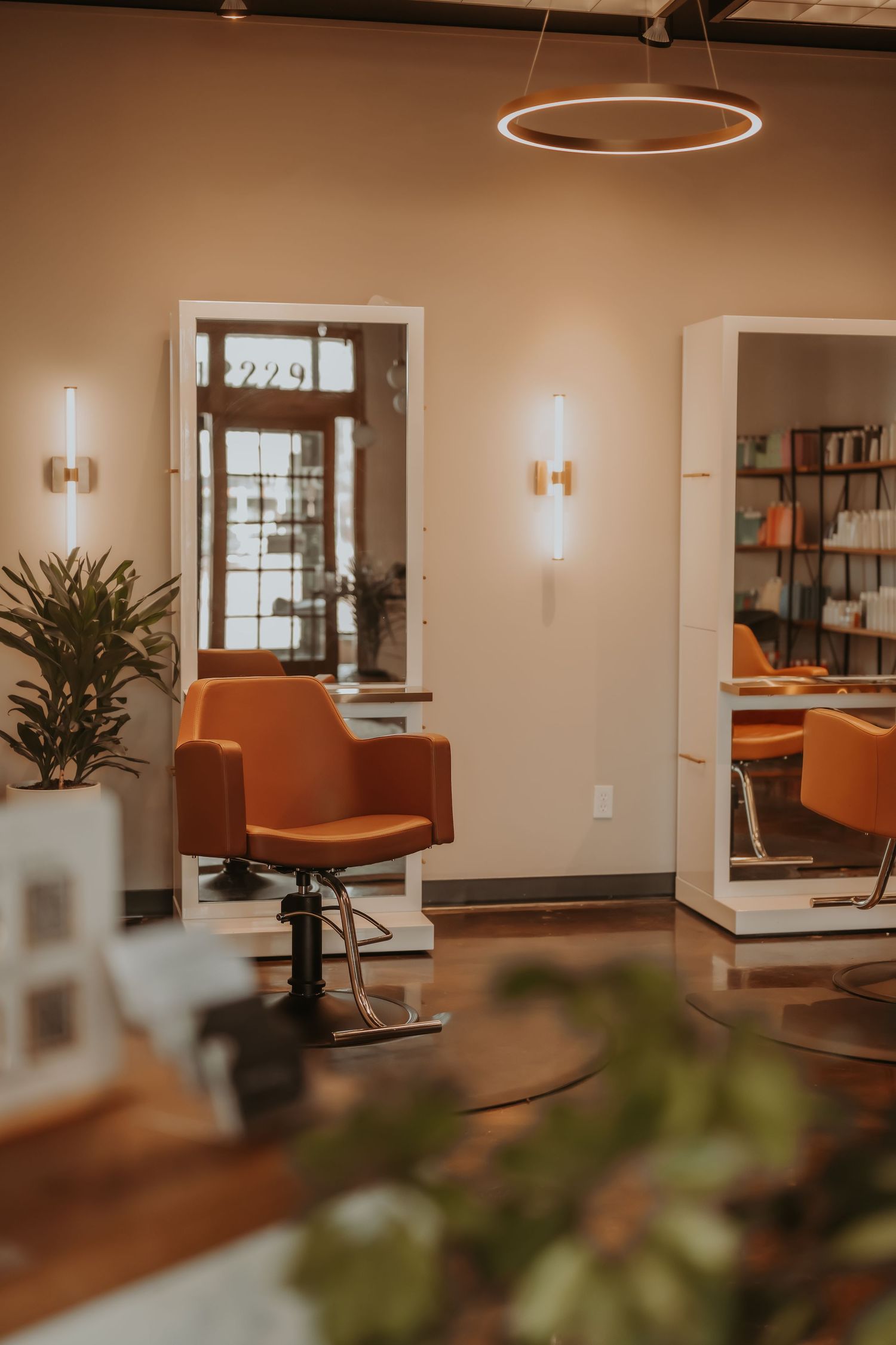 Modern salon interior with orange leather chairs, circular lighting fixture, and minimalist decor.