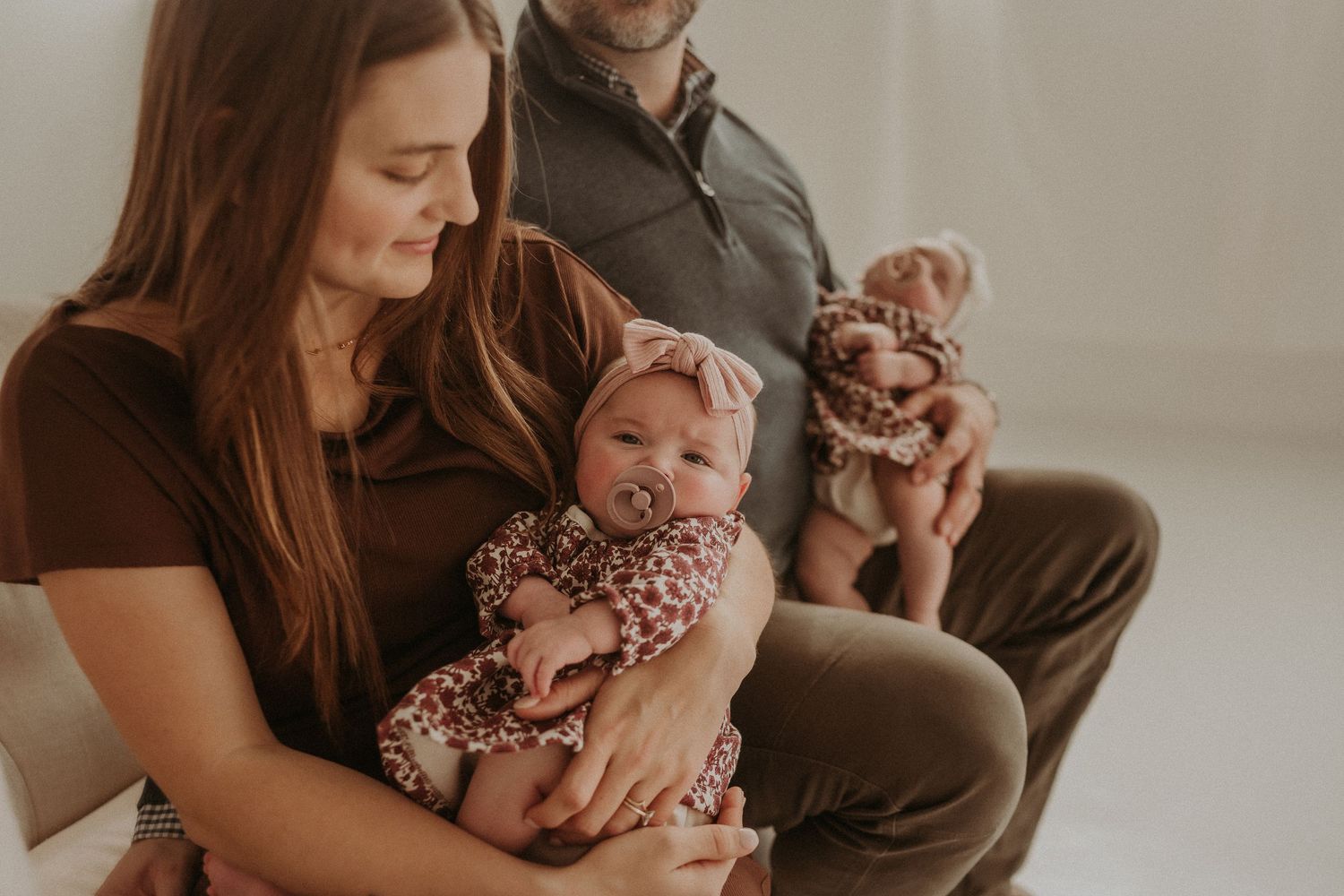 A family of three shares a tender moment with their baby wearing a floral dress.