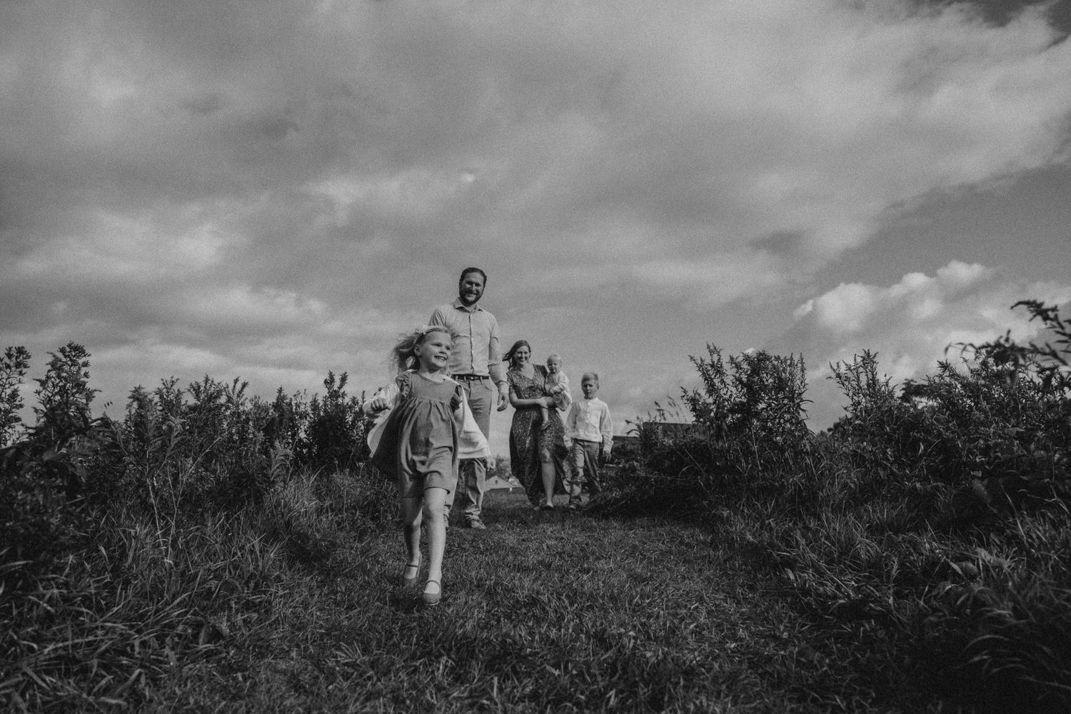 Black and white photo of a family running together on a grassy hillside path.