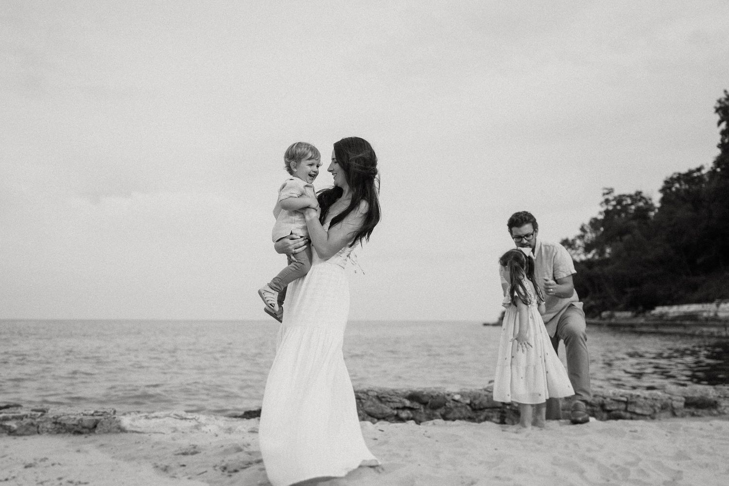 Family members pose along the rocky shoreline in elegant white attire.