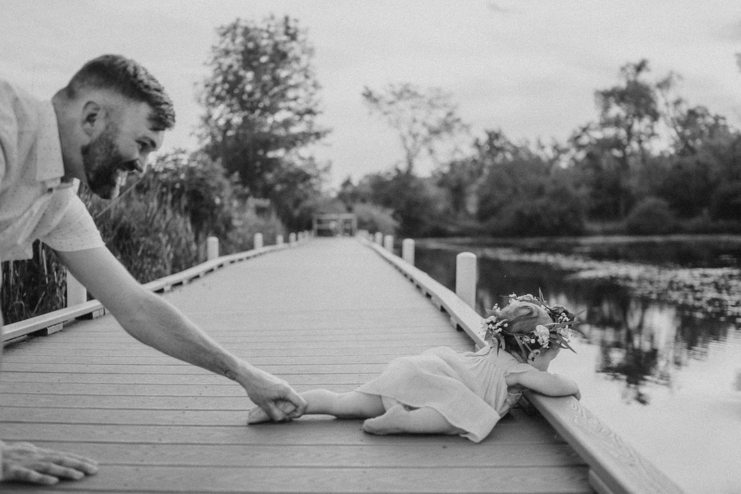 Black and white photo of playful interaction on a wooden boardwalk over water at sunset.