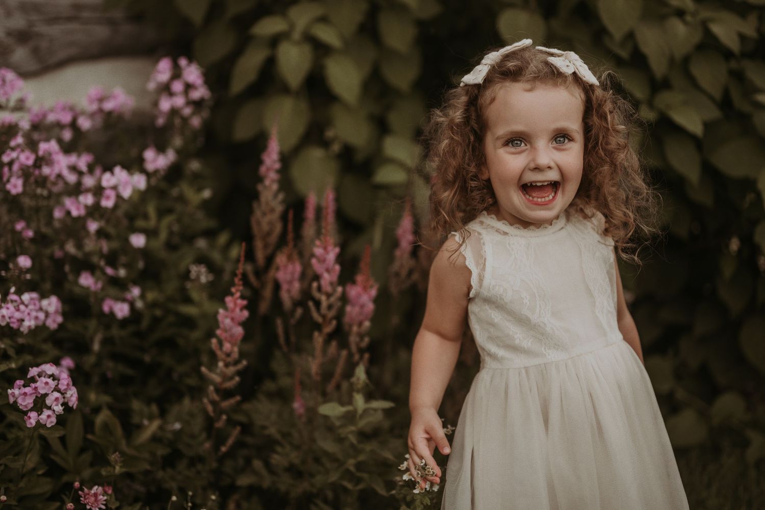 Warm lighting illuminates a cheerful garden scene with pink flowers and lush greenery.
