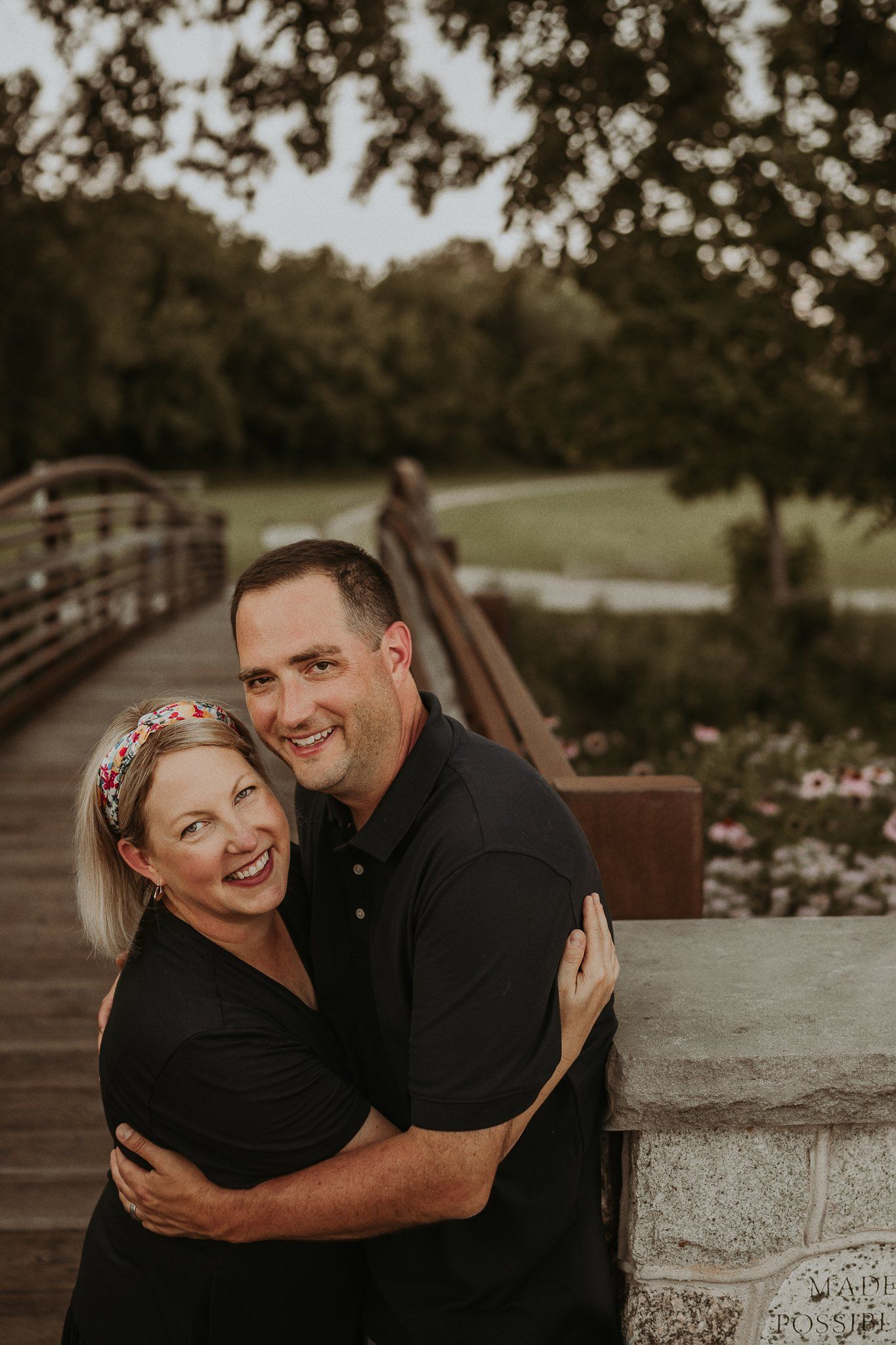 A happy couple embracing on a wooden bridge surrounded by lush greenery at sunset.
