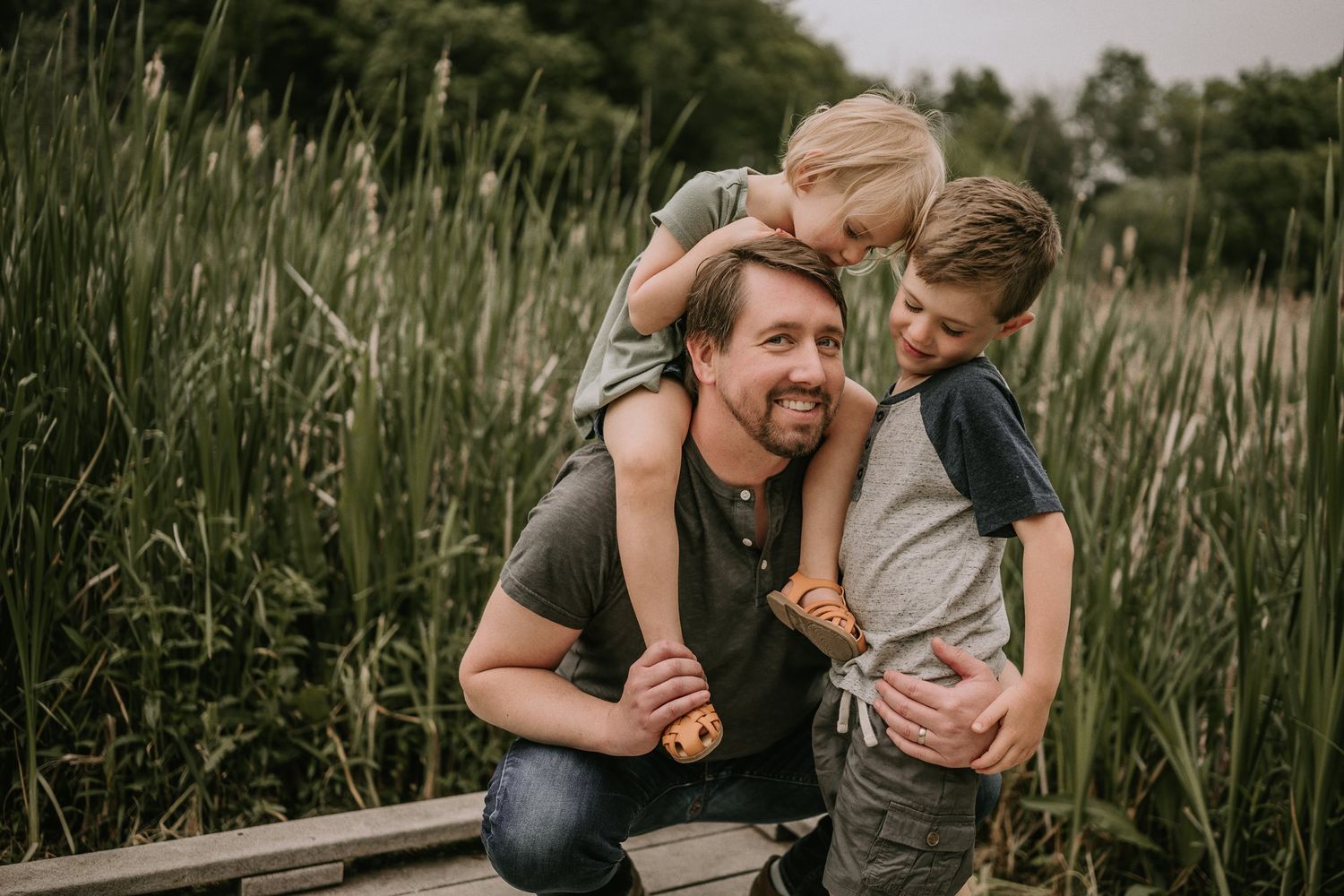 Joyful family moment captured on a wooden boardwalk surrounded by tall grass.
