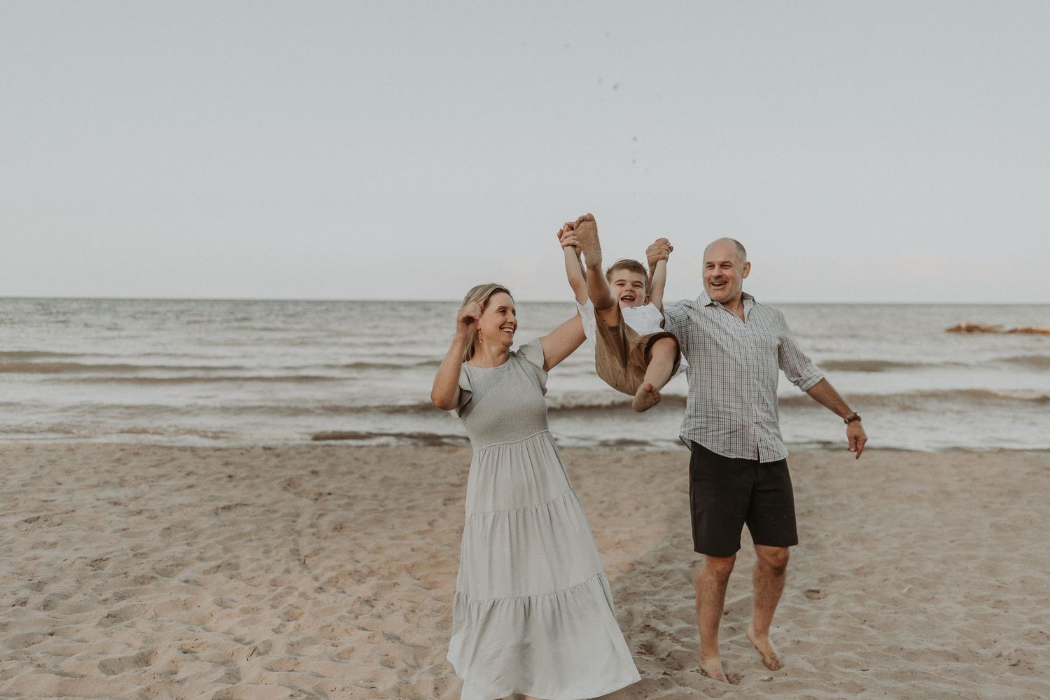 A joyful family moment captured on the beach with playful expressions and casual attire.